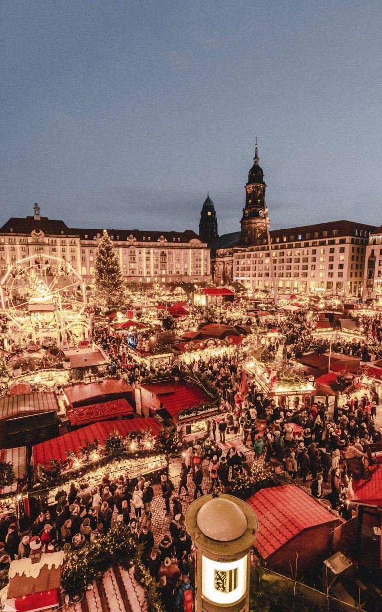 Christmas market in Dresden, Germany with a large crowd of people and a tall clock tower in the background. - Christmas