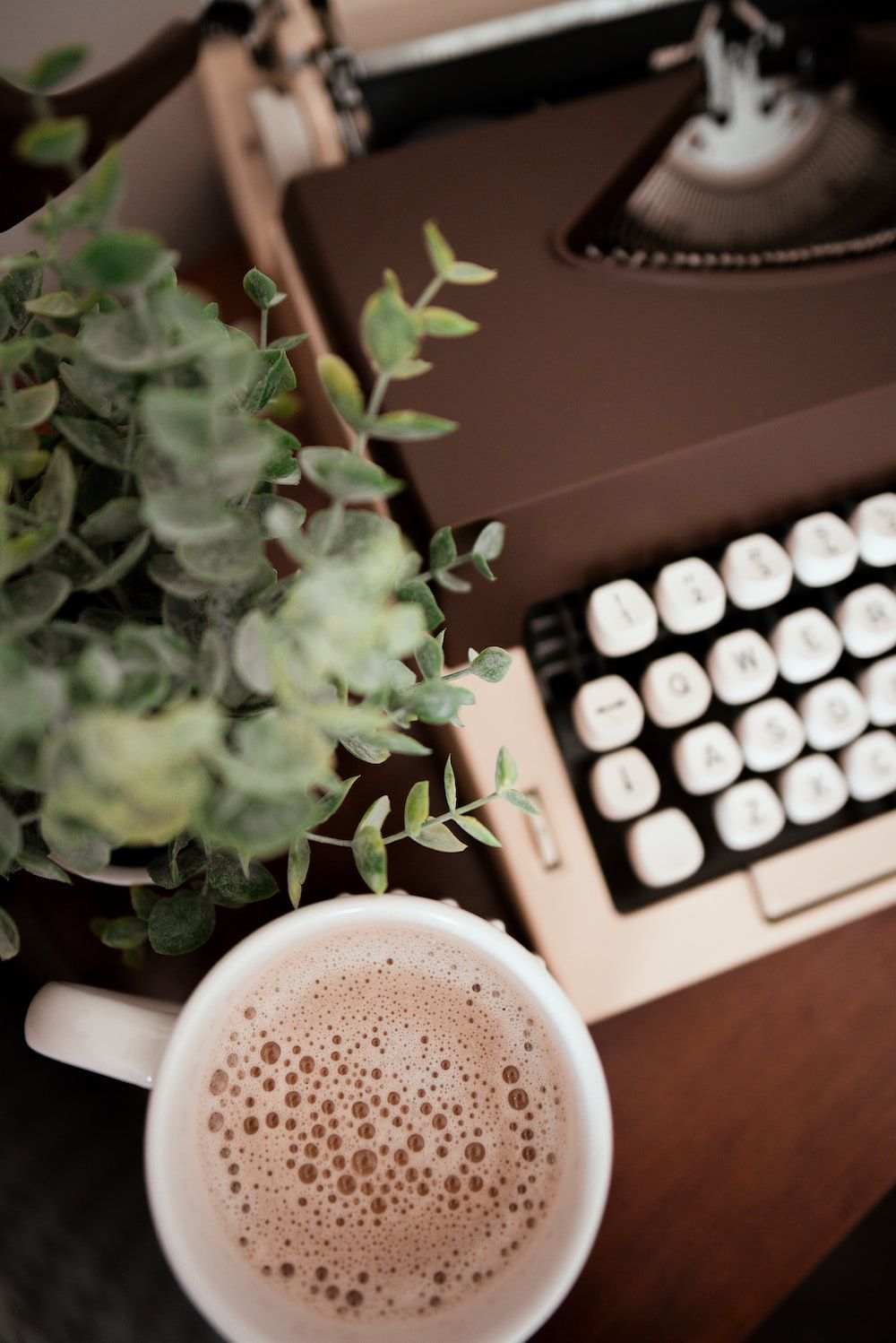 A cup of coffee next to a typewriter and a plant. - Coffee