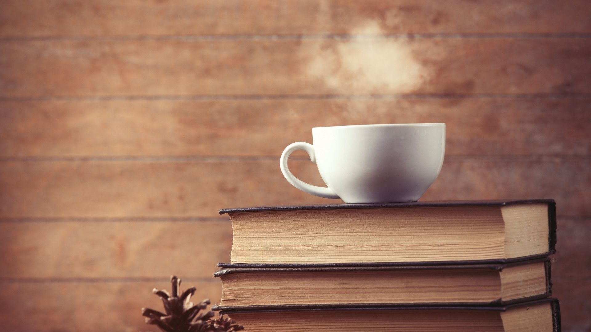 A steaming cup of coffee sitting on top of a stack of books. - Coffee
