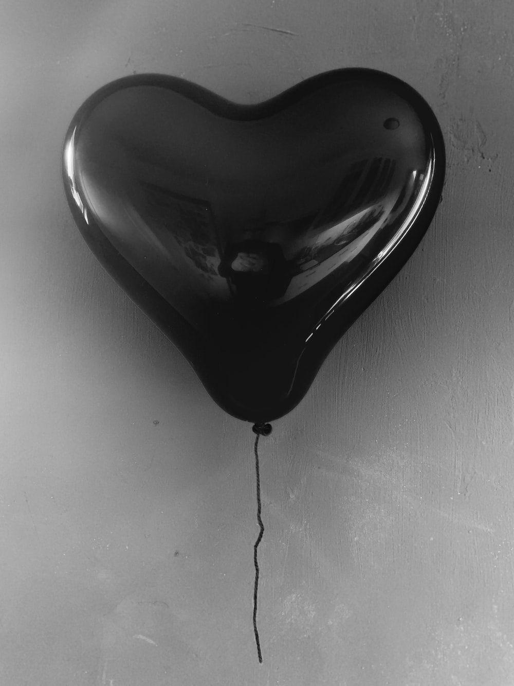 A black heart balloon is tied to a string and is about to pop. - Black heart