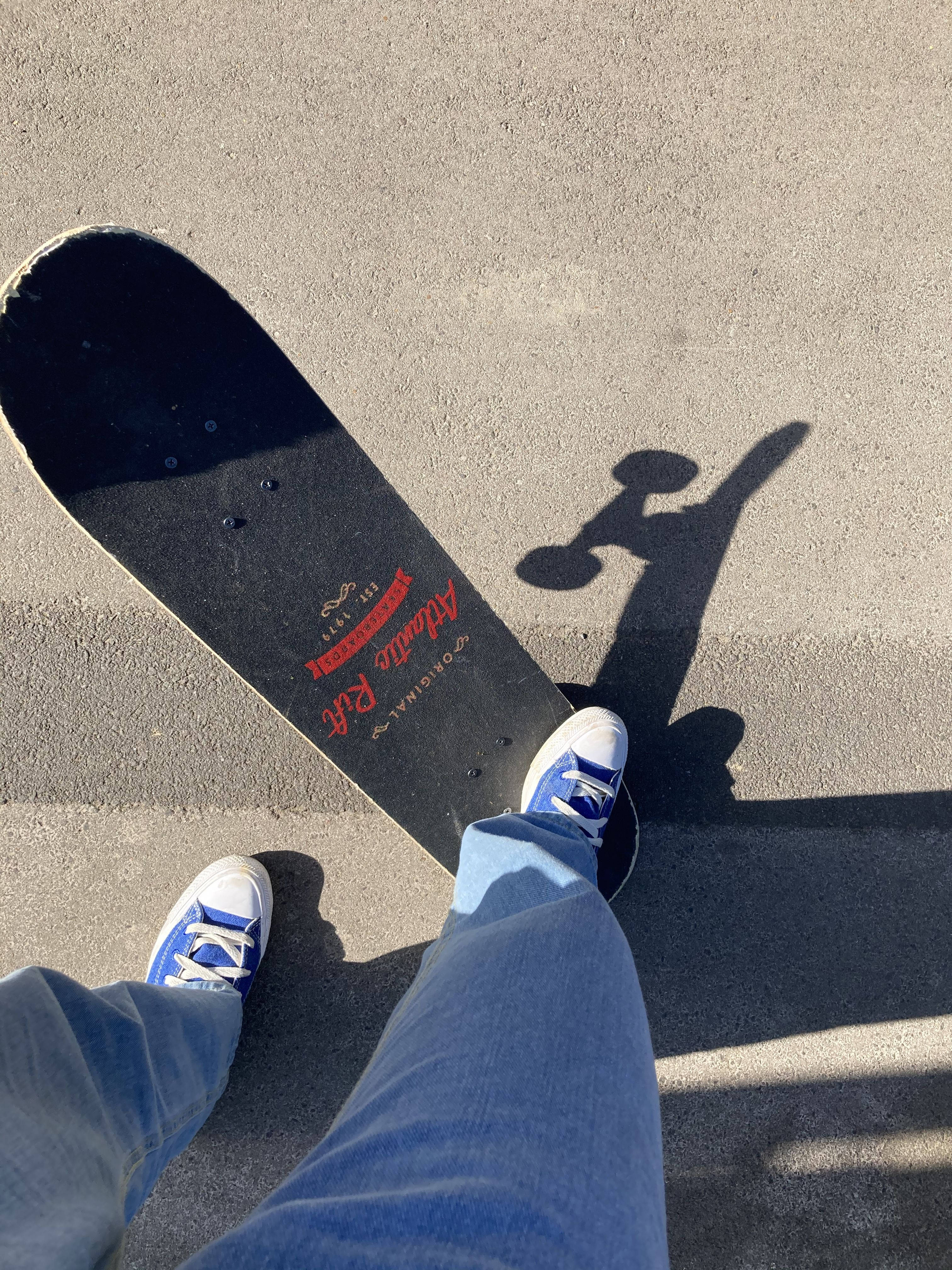 A person wearing blue jeans and blue and white shoes stands in front of a skateboard. - Skate, skater