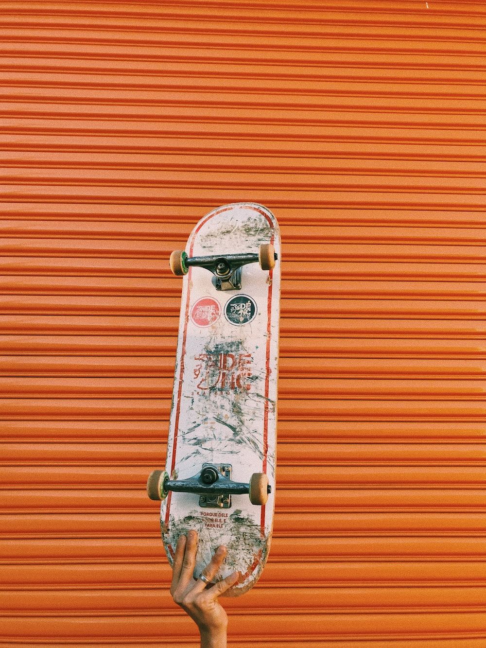 Person holding skateboard in front of the orange wall - Skate