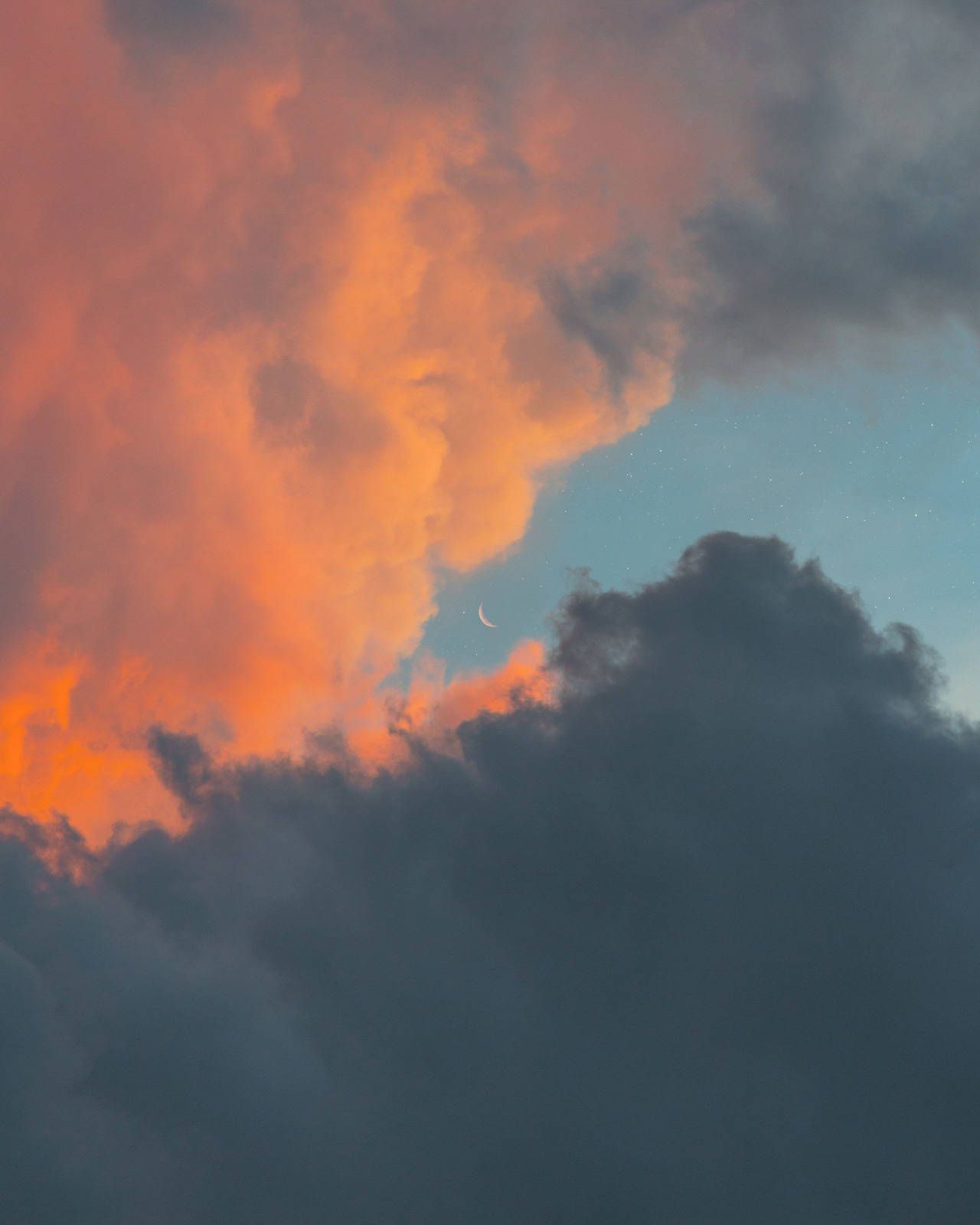 A crescent moon is peeking out from behind a cloud in a sky that is half orange and half blue. - Vintage clouds