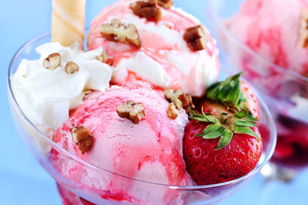 A bowl of strawberry ice cream with nuts and whipped cream. - Ice cream