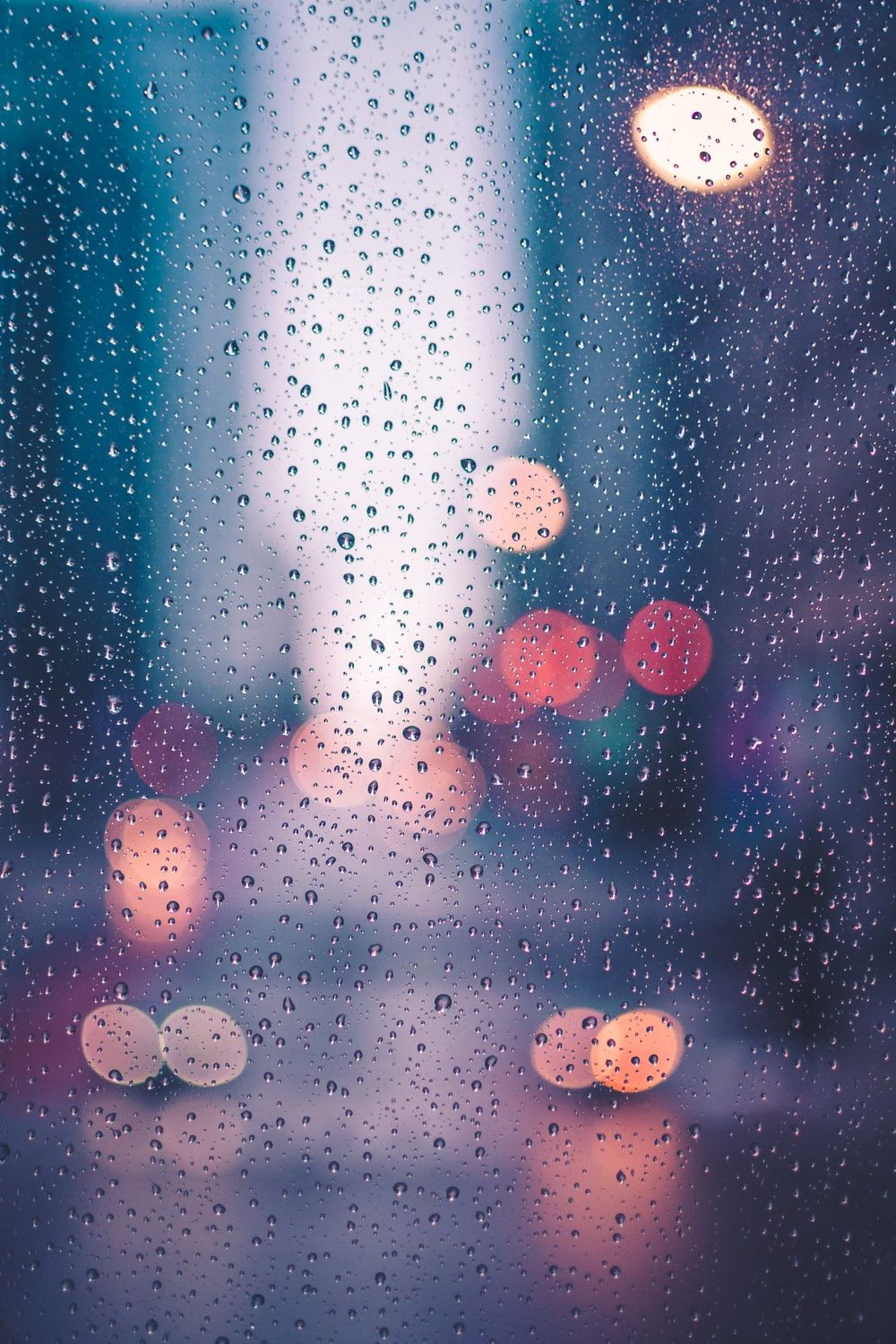 A rain covered window with city lights in the background - Rain