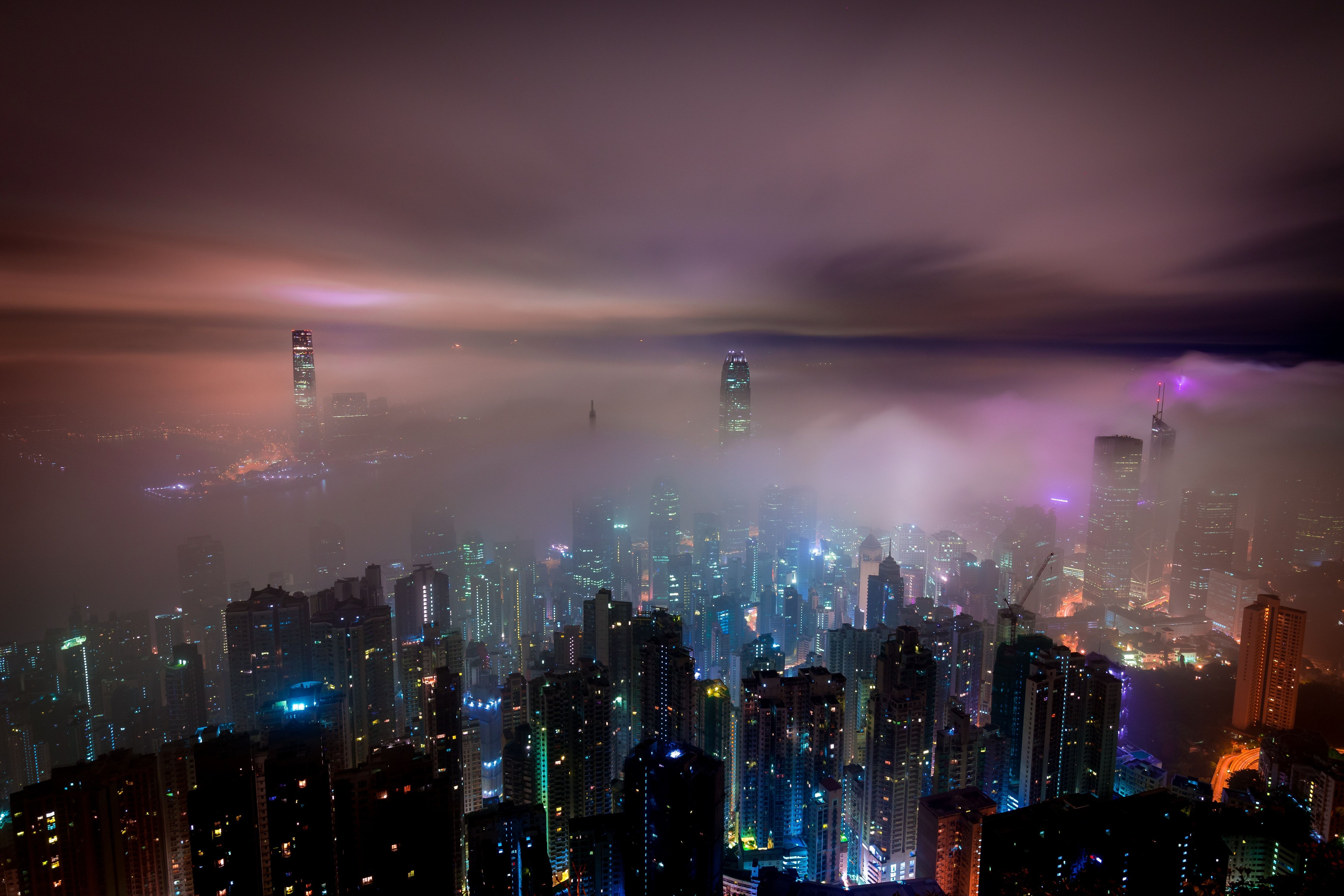 A city skyline at night with fog rolling through the buildings. - Night