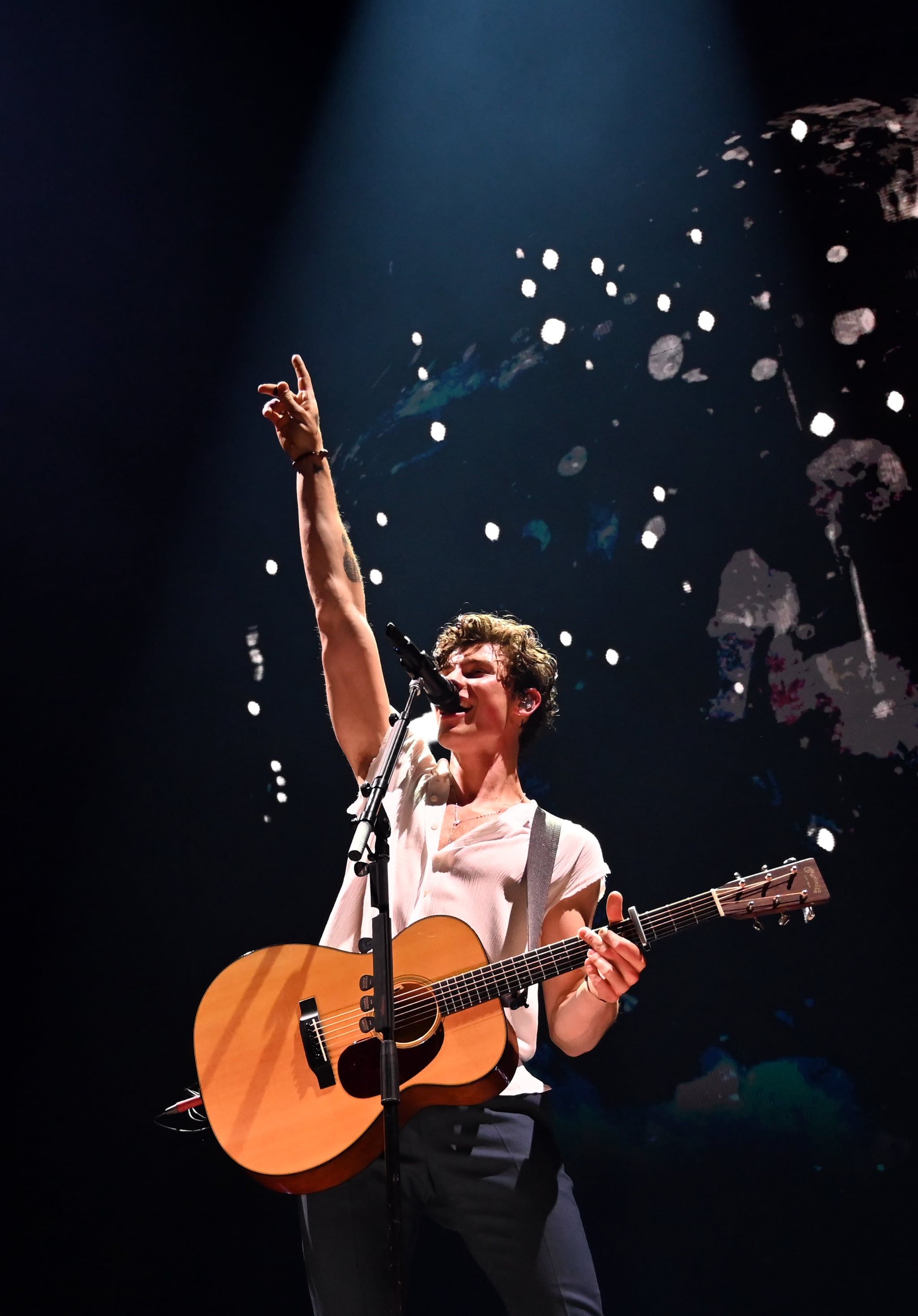 A man holding an acoustic guitar on stage - Shawn Mendes