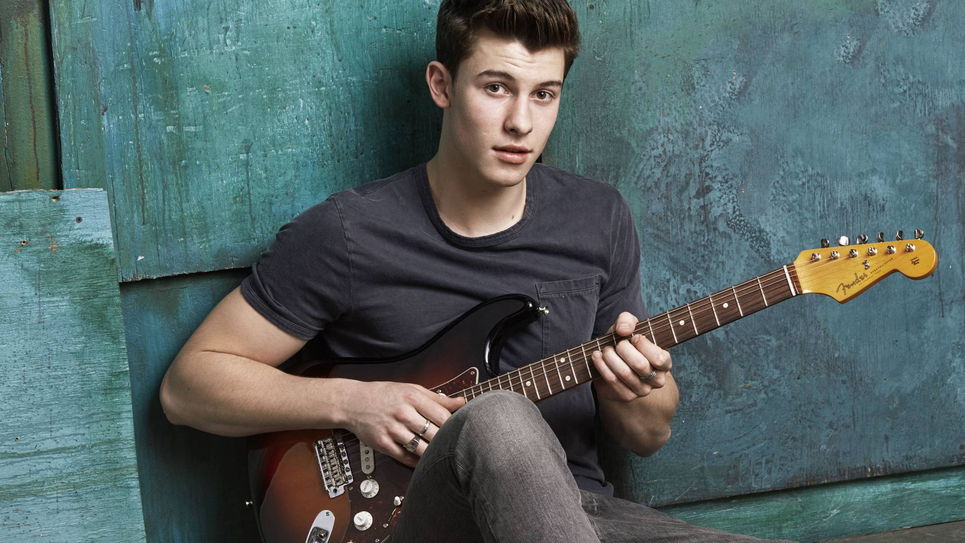 A young man sitting on the ground playing guitar - Shawn Mendes