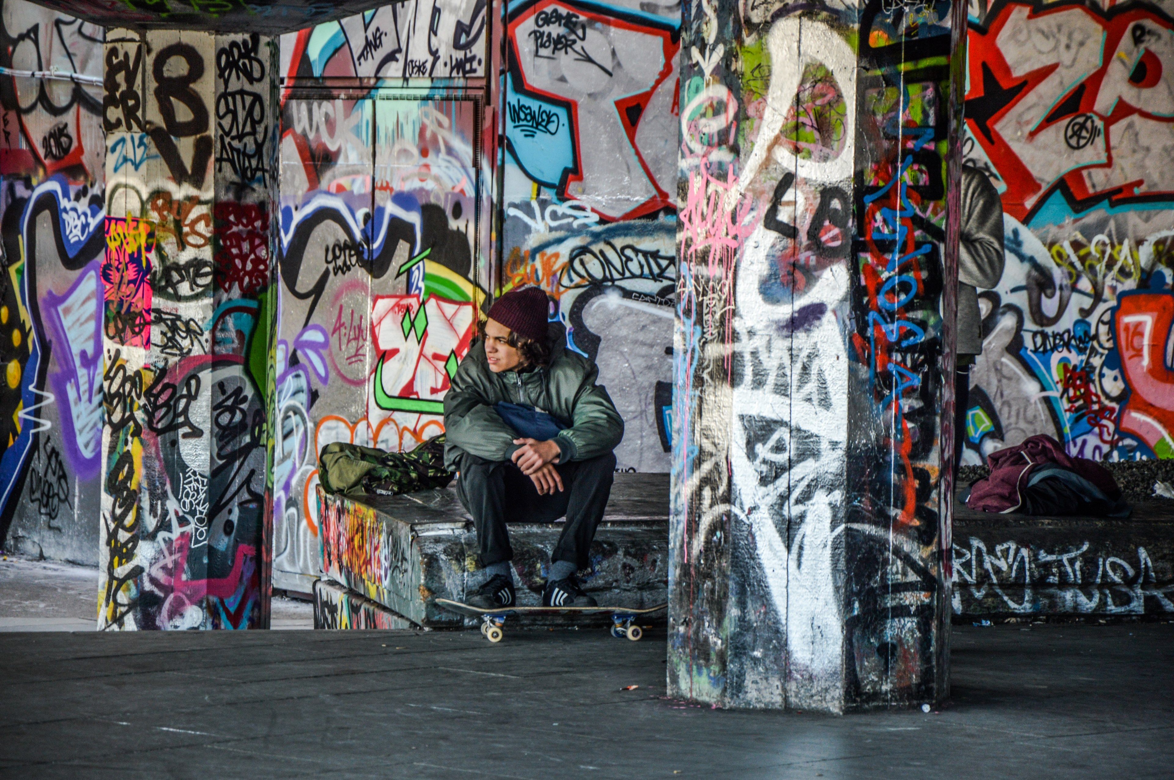 Wallpaper / young man with skateboard sitting in urban area with walls covered in colorful graffiti london, a skater sits around graffiti 4k wallpaper free download