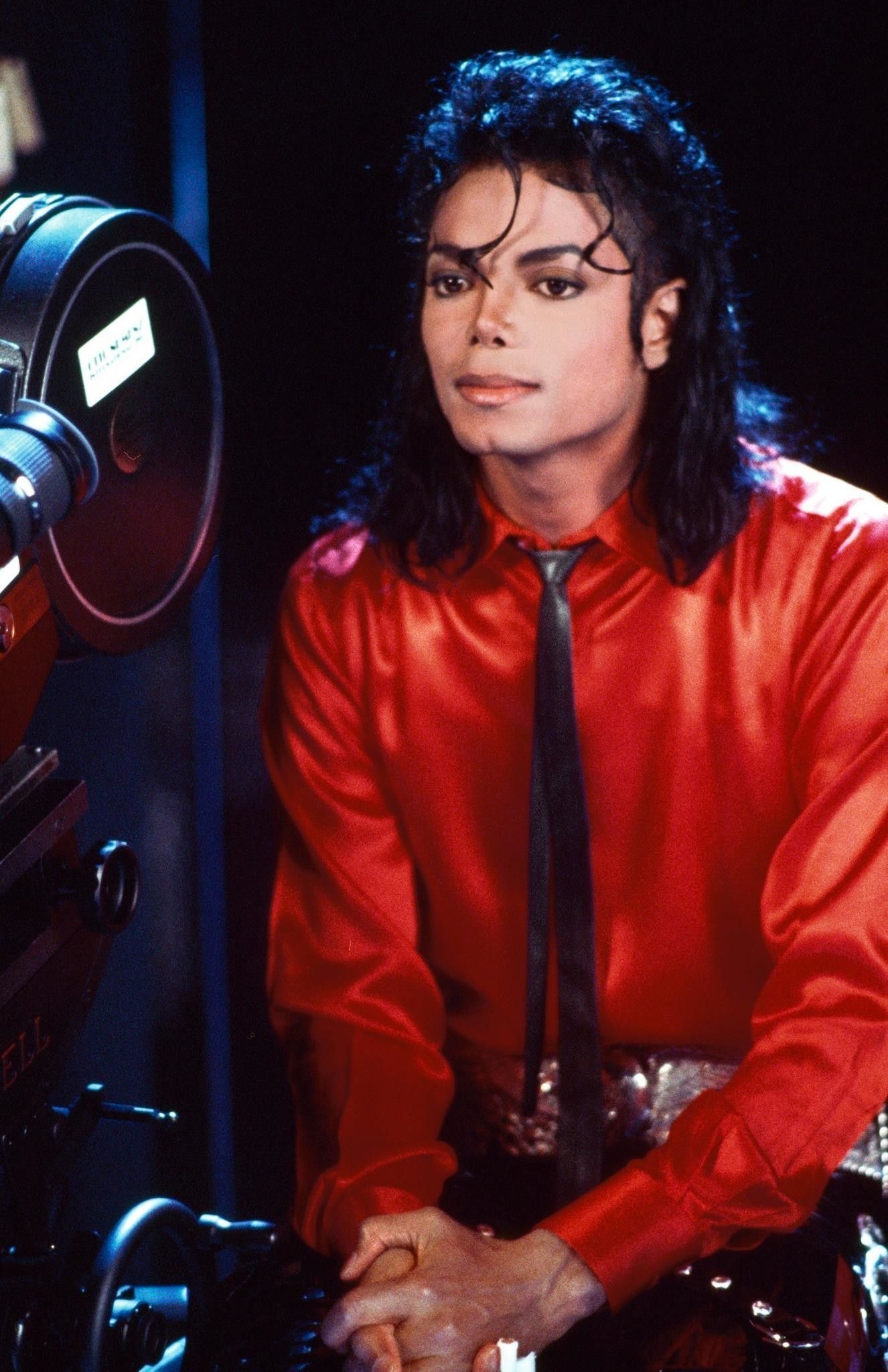 A man in red shirt and tie sitting next to camera - Michael Jackson