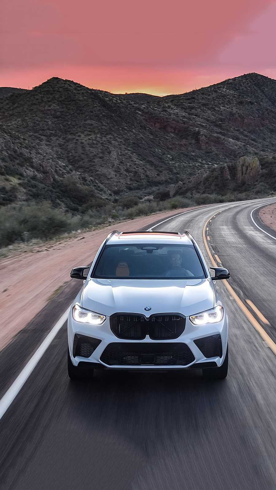 A white BMW X6 M Competition driving down a mountain road - BMW