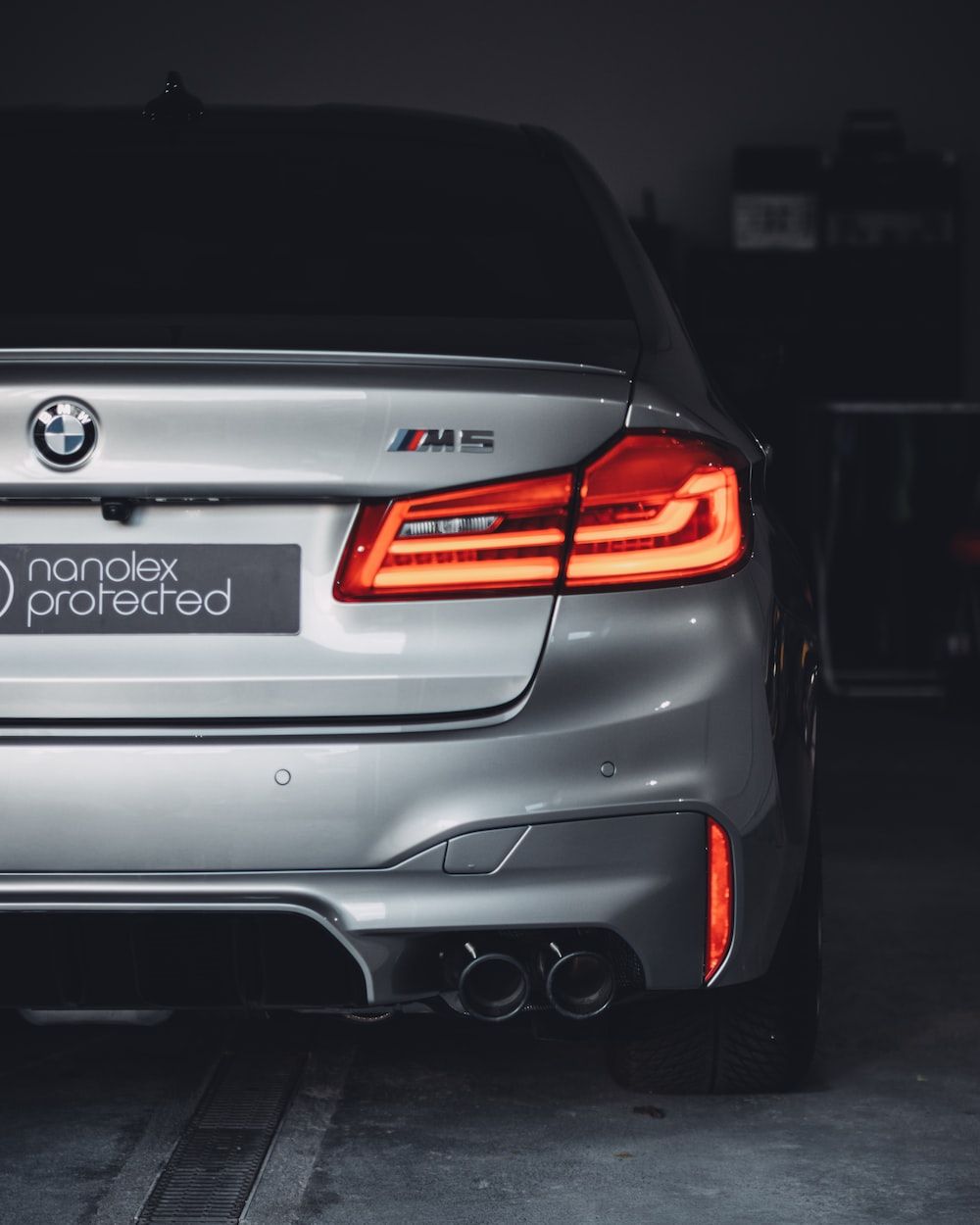 The back end of a silver BMW M5 with a dark background. - BMW