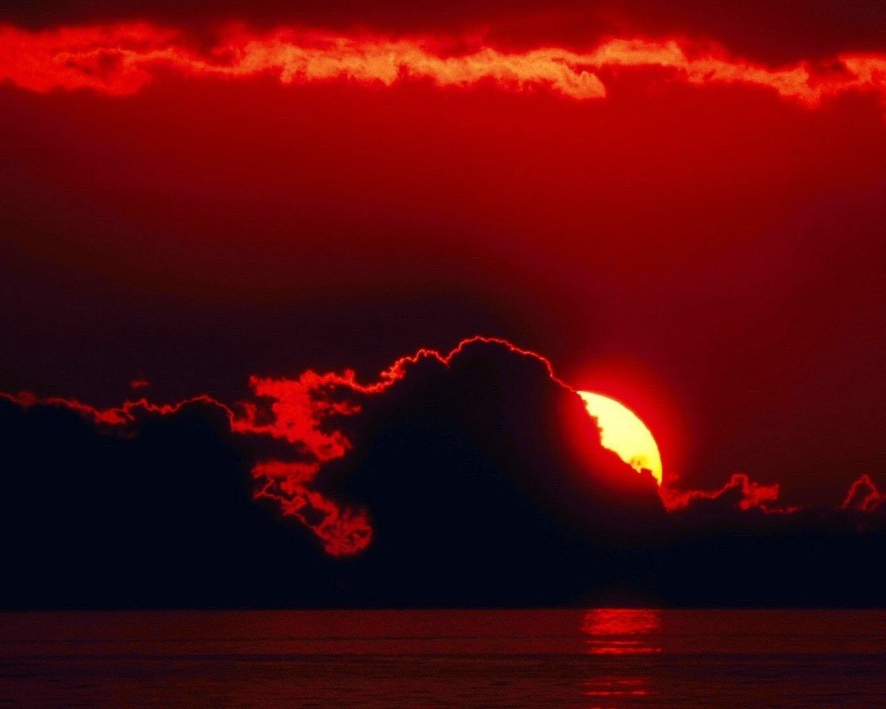A red sun setting behind clouds and water - Crimson