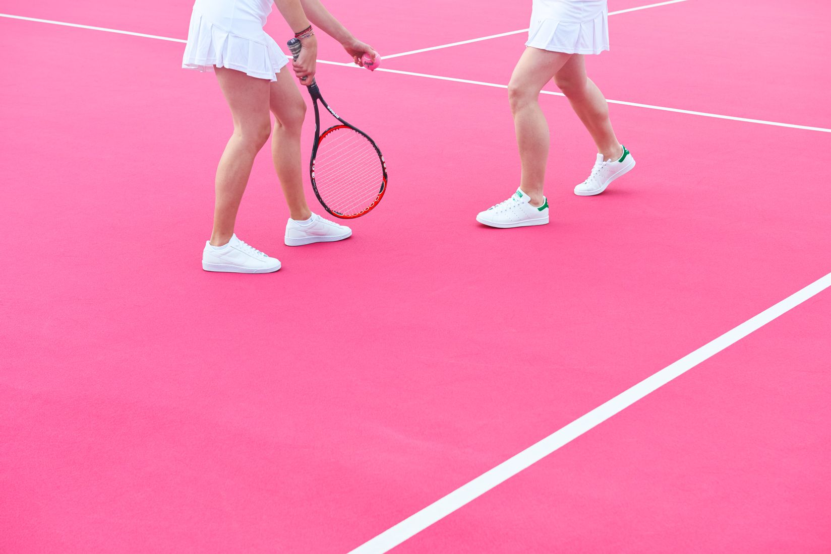 Two women in white tennis outfits on a pink court - Tennis