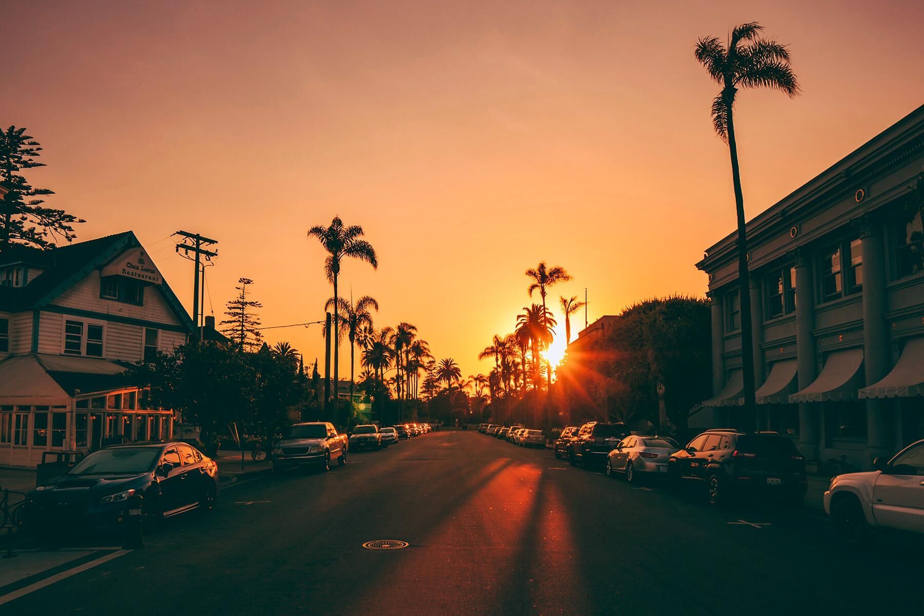 A street in California with palm trees and cars parked on the side of the road. - Sunset