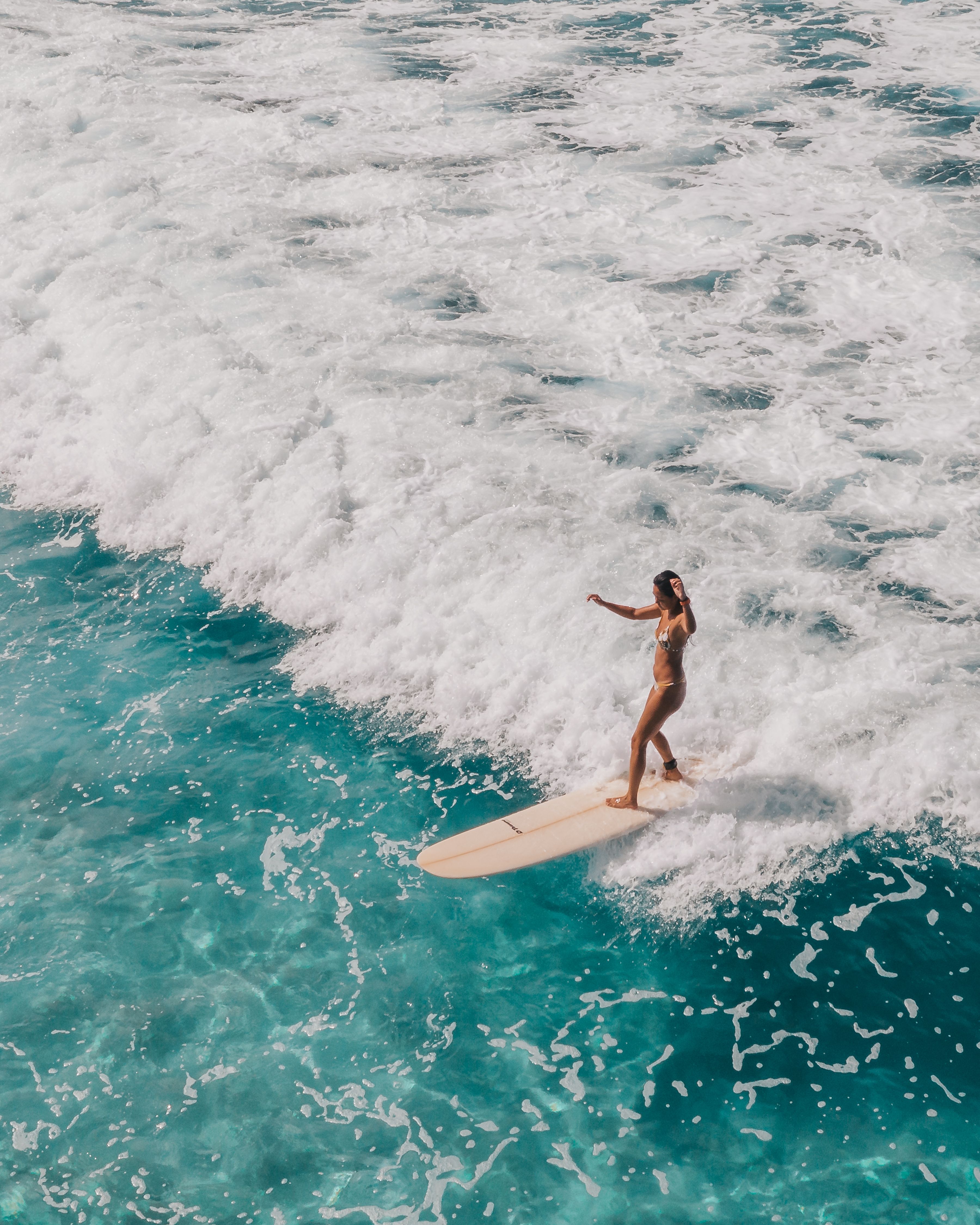 A woman in a bikini stands on a surfboard riding a wave. - Surf