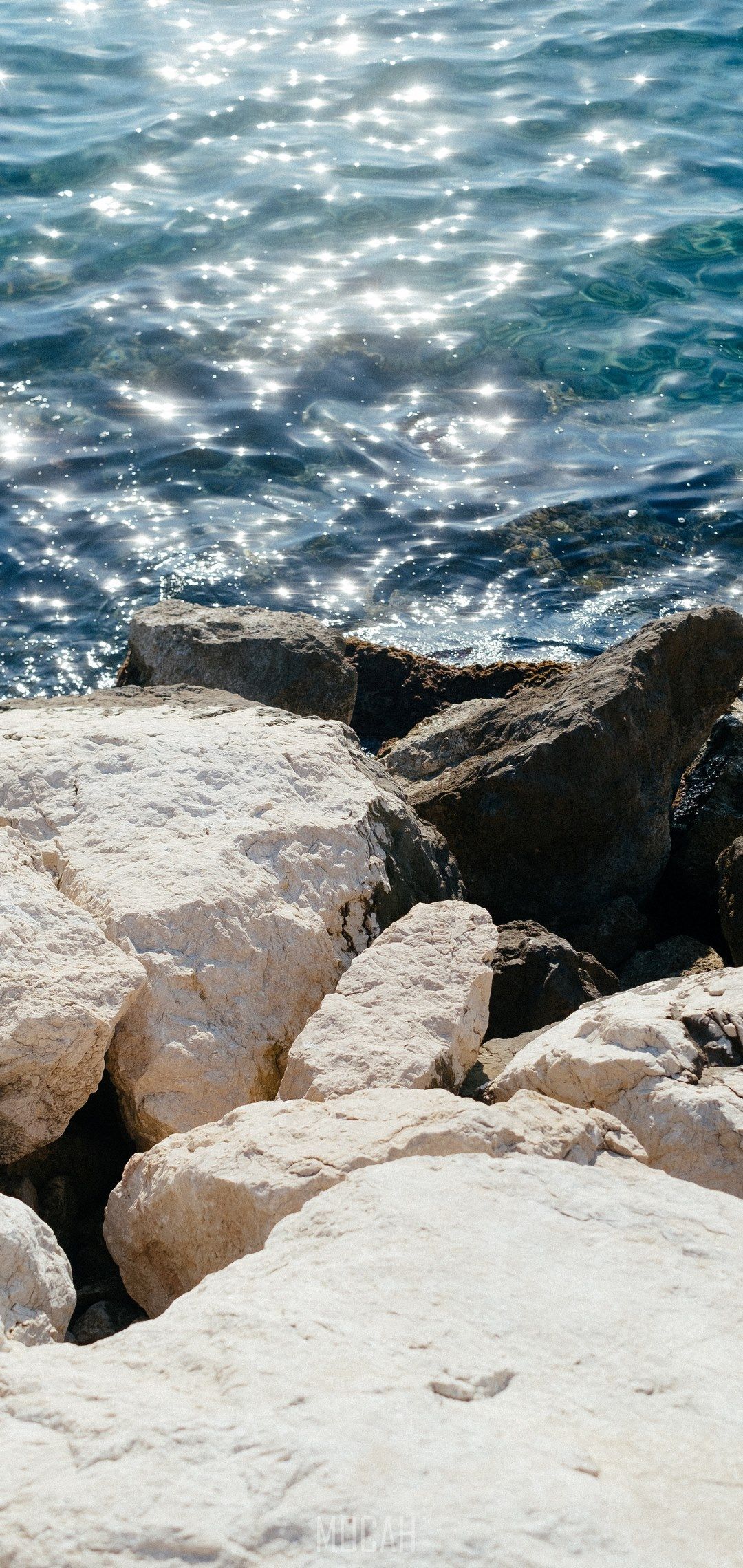 A person sitting on the rocks by water - Beach