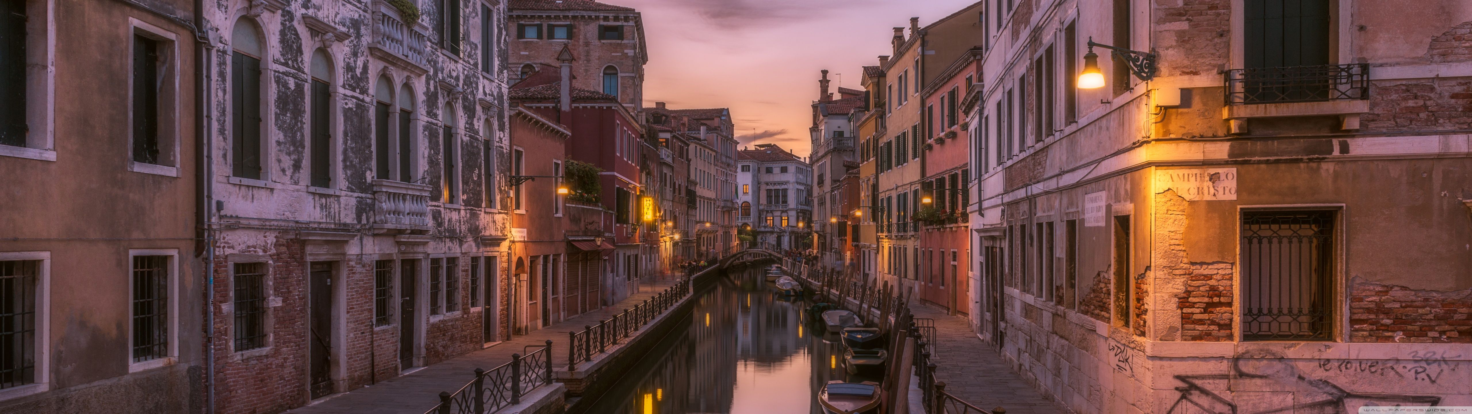 Boats are docked on the side of a canal in a city. - Italy