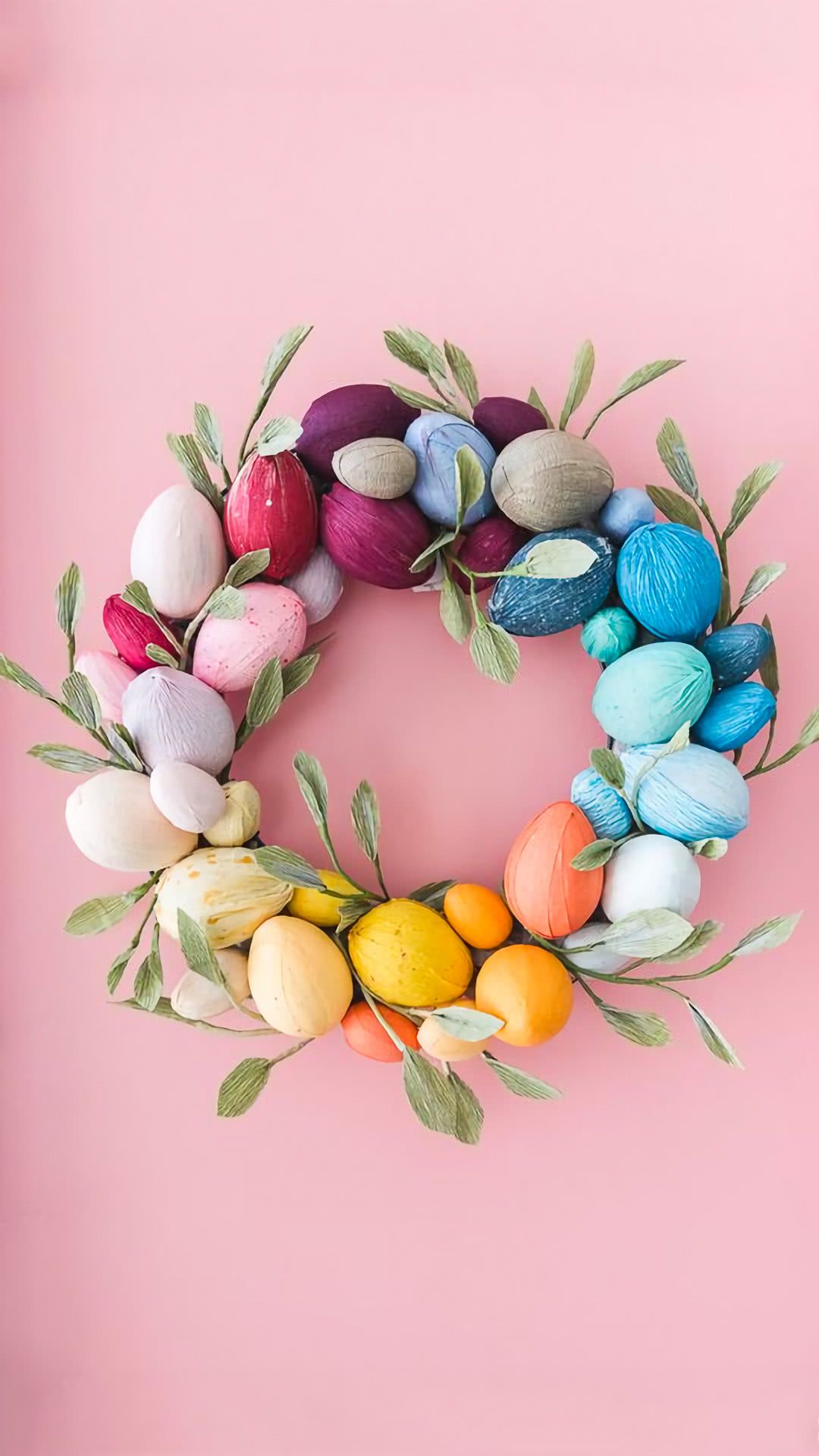 Easter wreath made of painted eggs and green leaves on a pink background - Easter