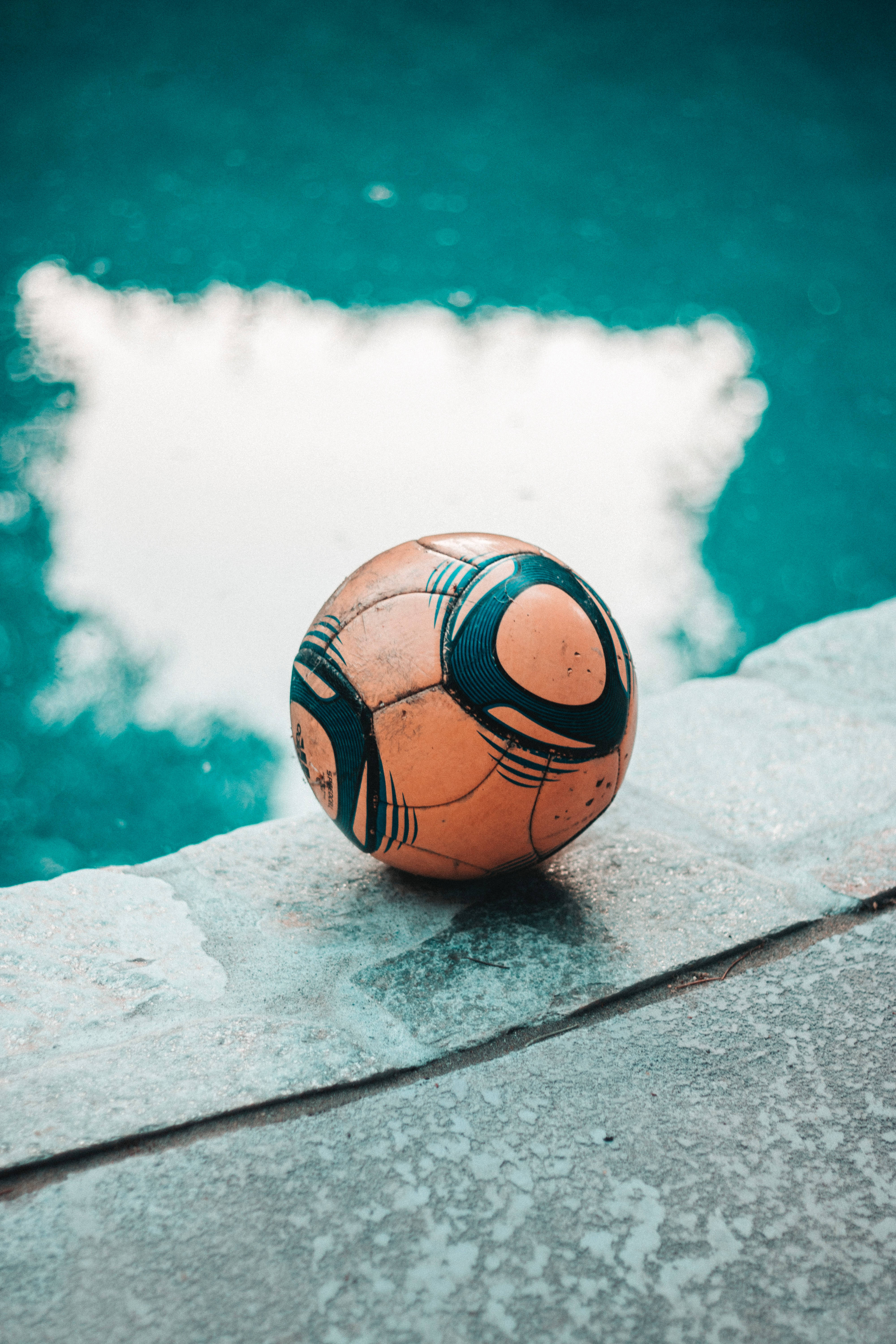 A soccer ball sitting on the edge of a pool. - Soccer