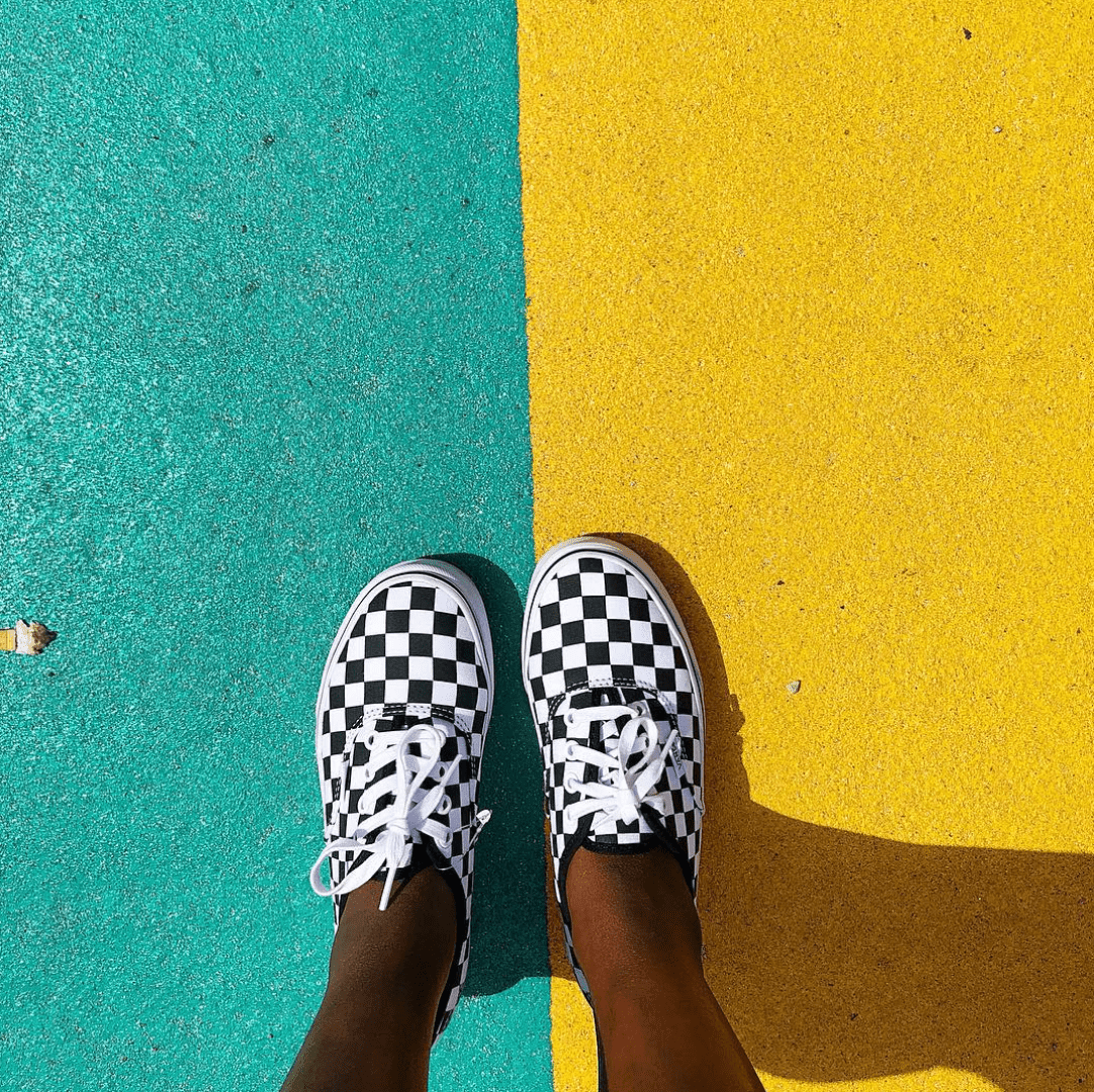 A person wearing checkered Vans sneakers standing on a yellow and green sidewalk. - Vans