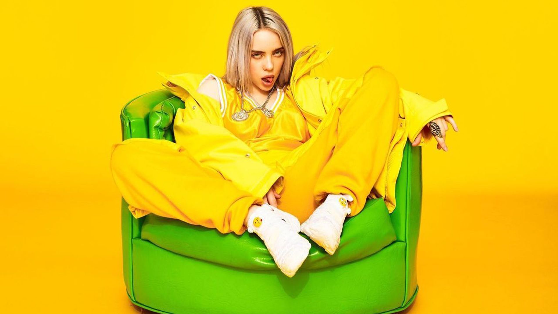 A woman in yellow sitting on top of green chair - Billie Eilish