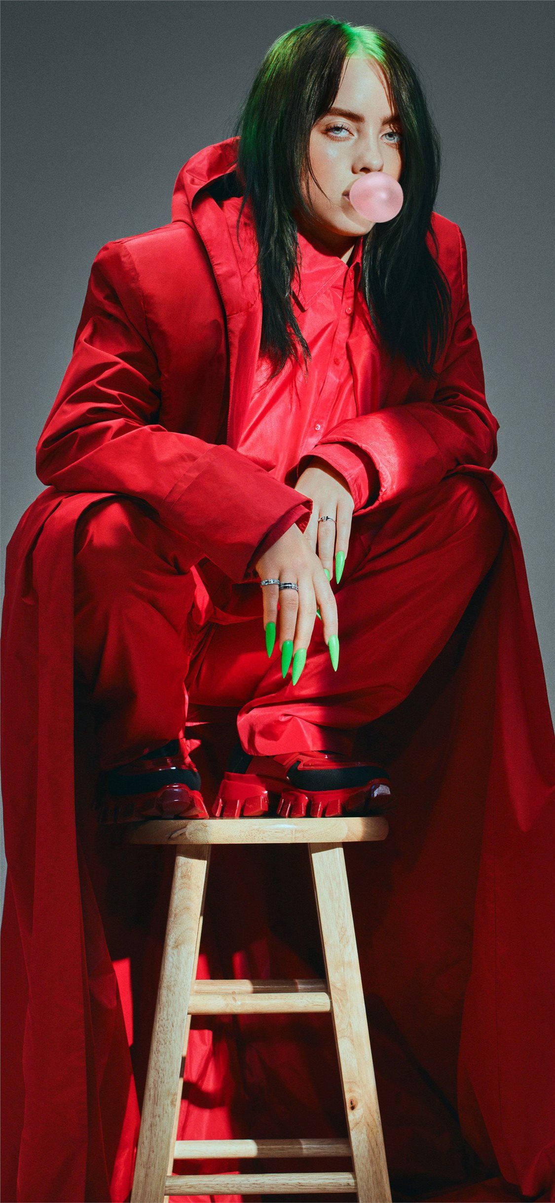 A person sitting on top of stool in red - Billie Eilish