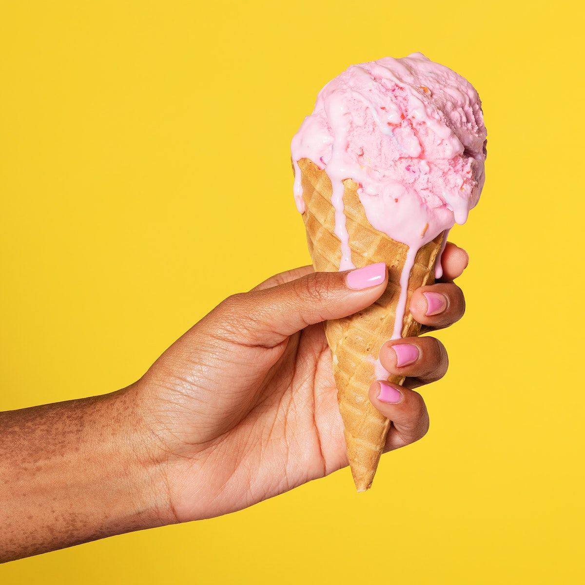 A person holding an ice cream cone with pink and white sprinks on it - Ice cream