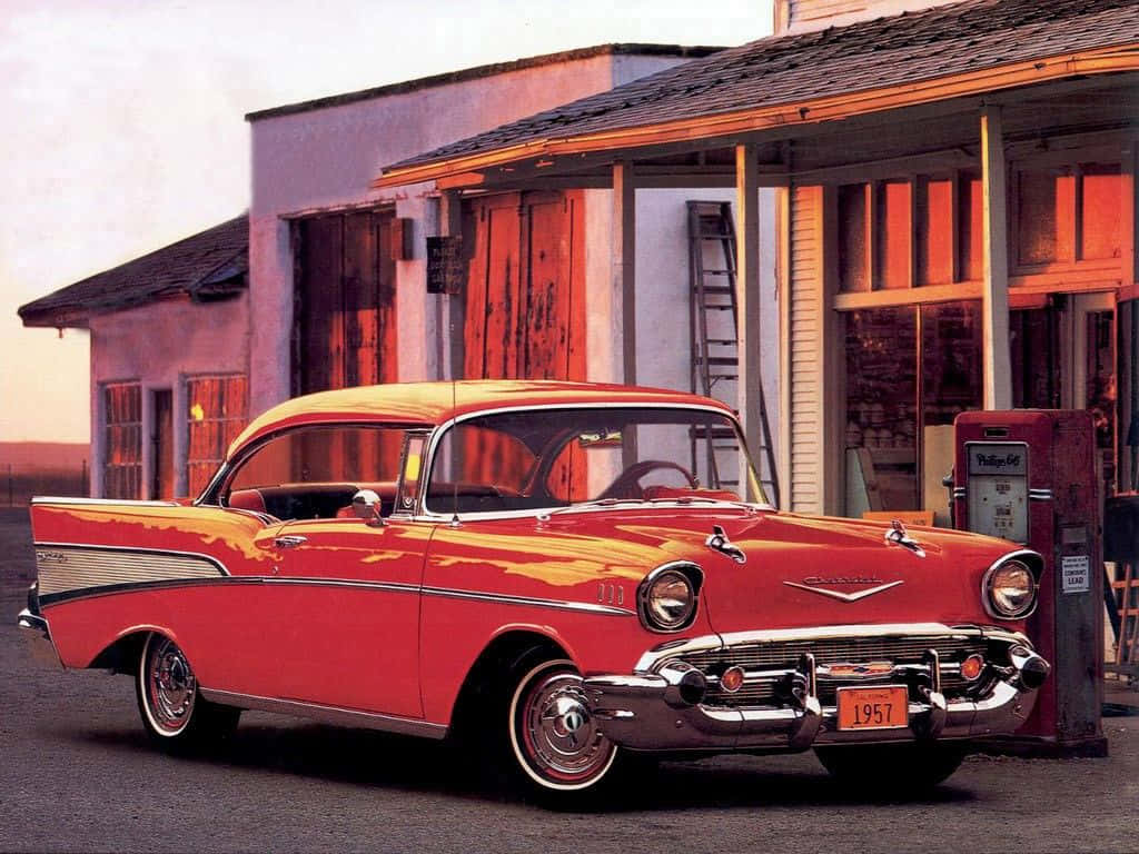A red and white 1957 Chevrolet Bel Air sits in front of a gas station. - 60s, 50s