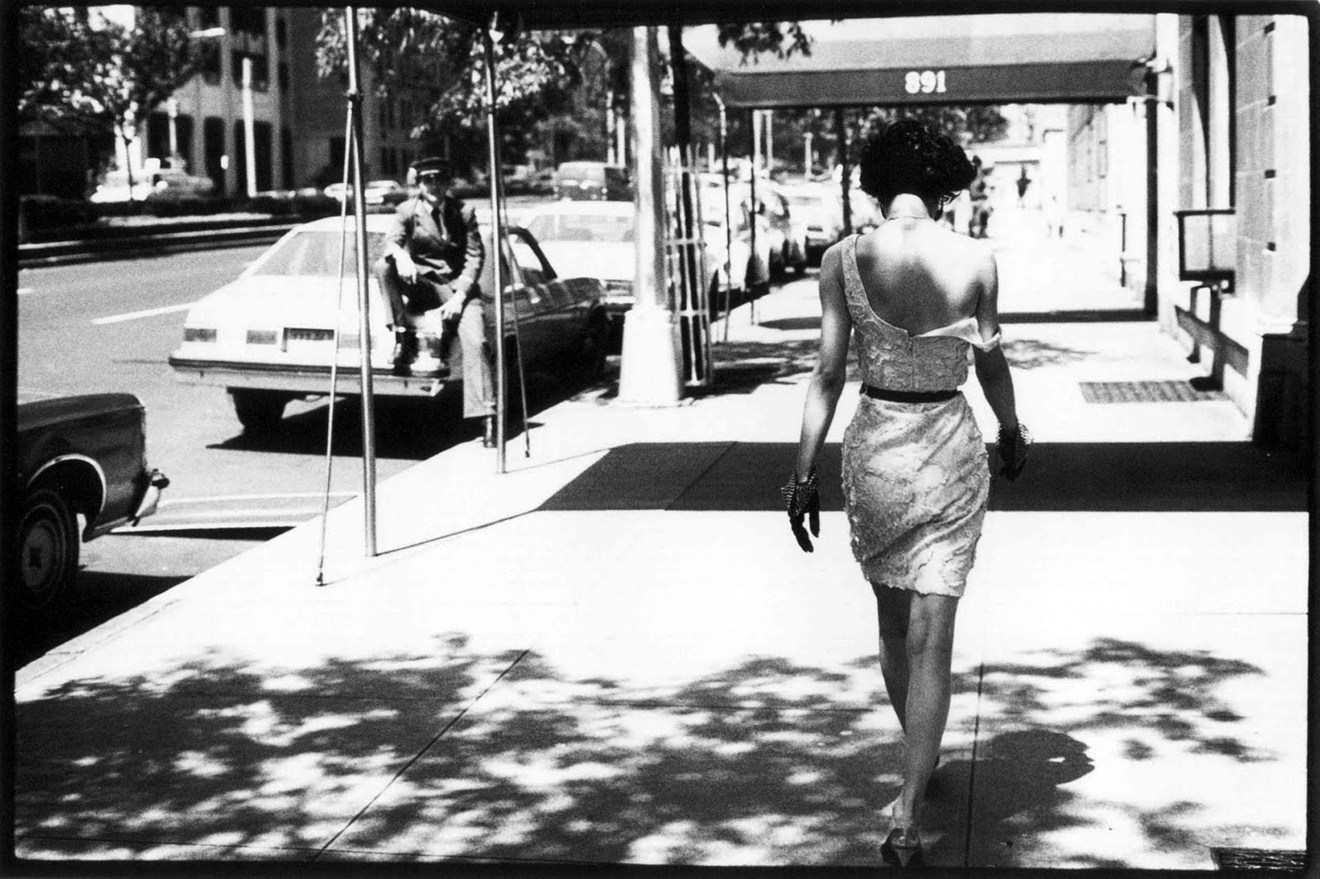 A woman walking down the street in front of a store window. - 60s