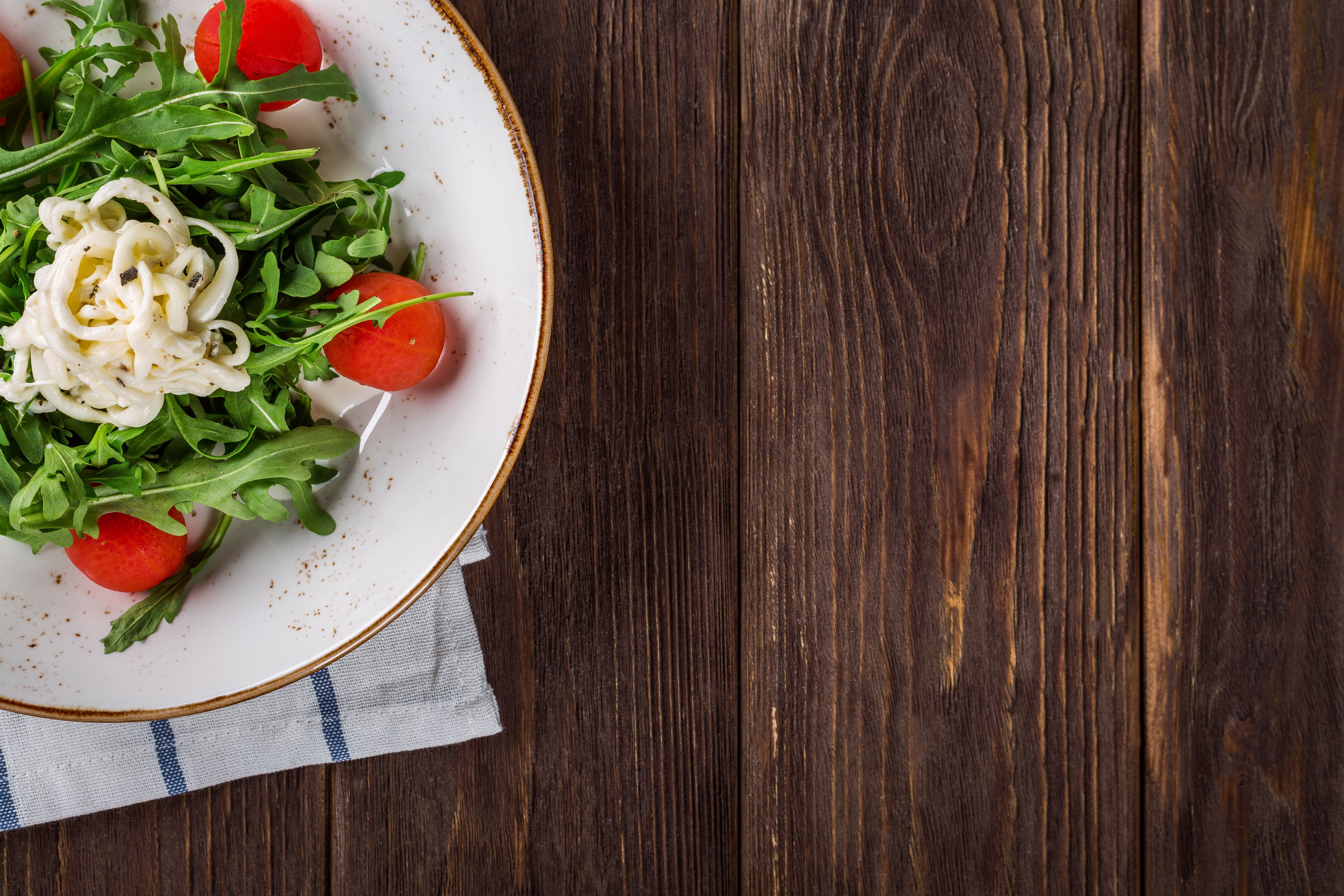A white plate with a salad of tomatoes, onions, and greens on a wooden table. - Food, foodie