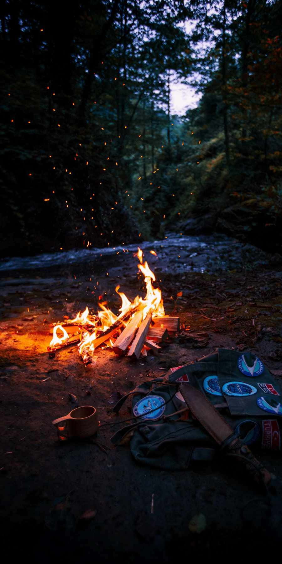 A campfire in the woods with the woods surrounding it. - Camping