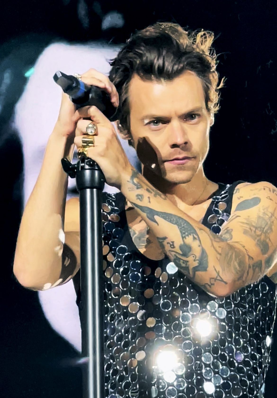 A man holding up his microphone with tattoos on both arms - Harry Styles