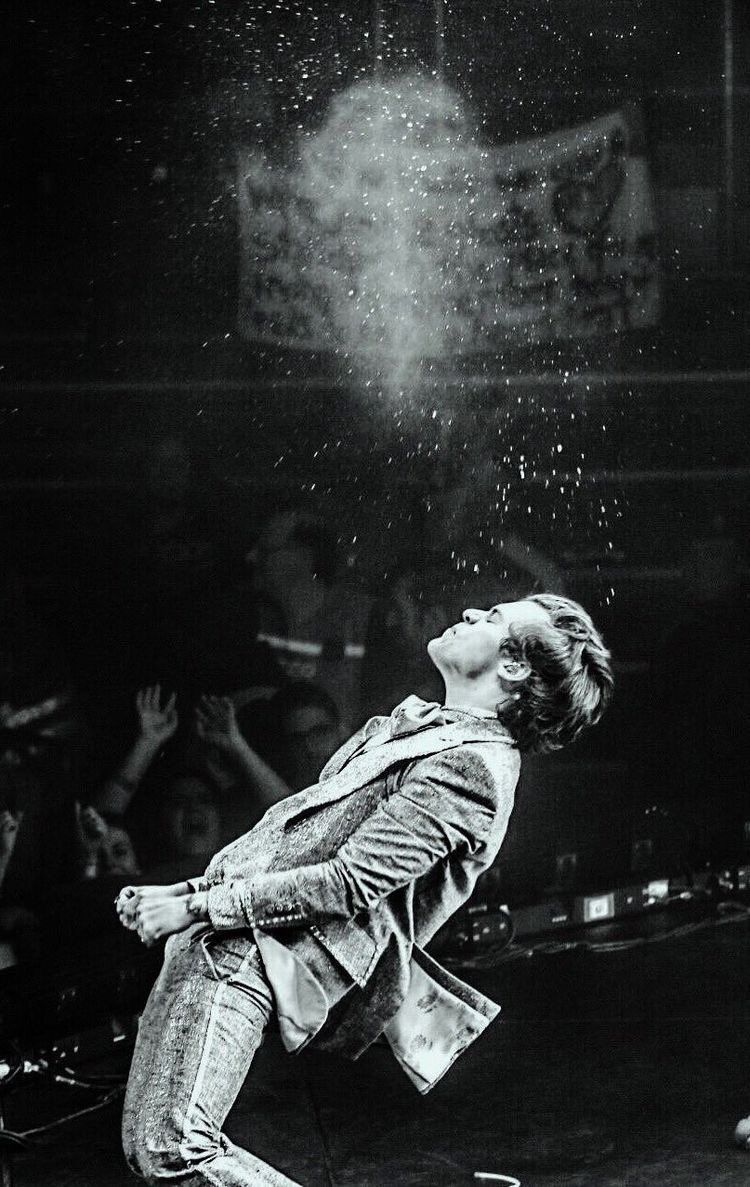 The artist, Harry Styles, in a suit, throws water in the air during a performance. - Harry Styles
