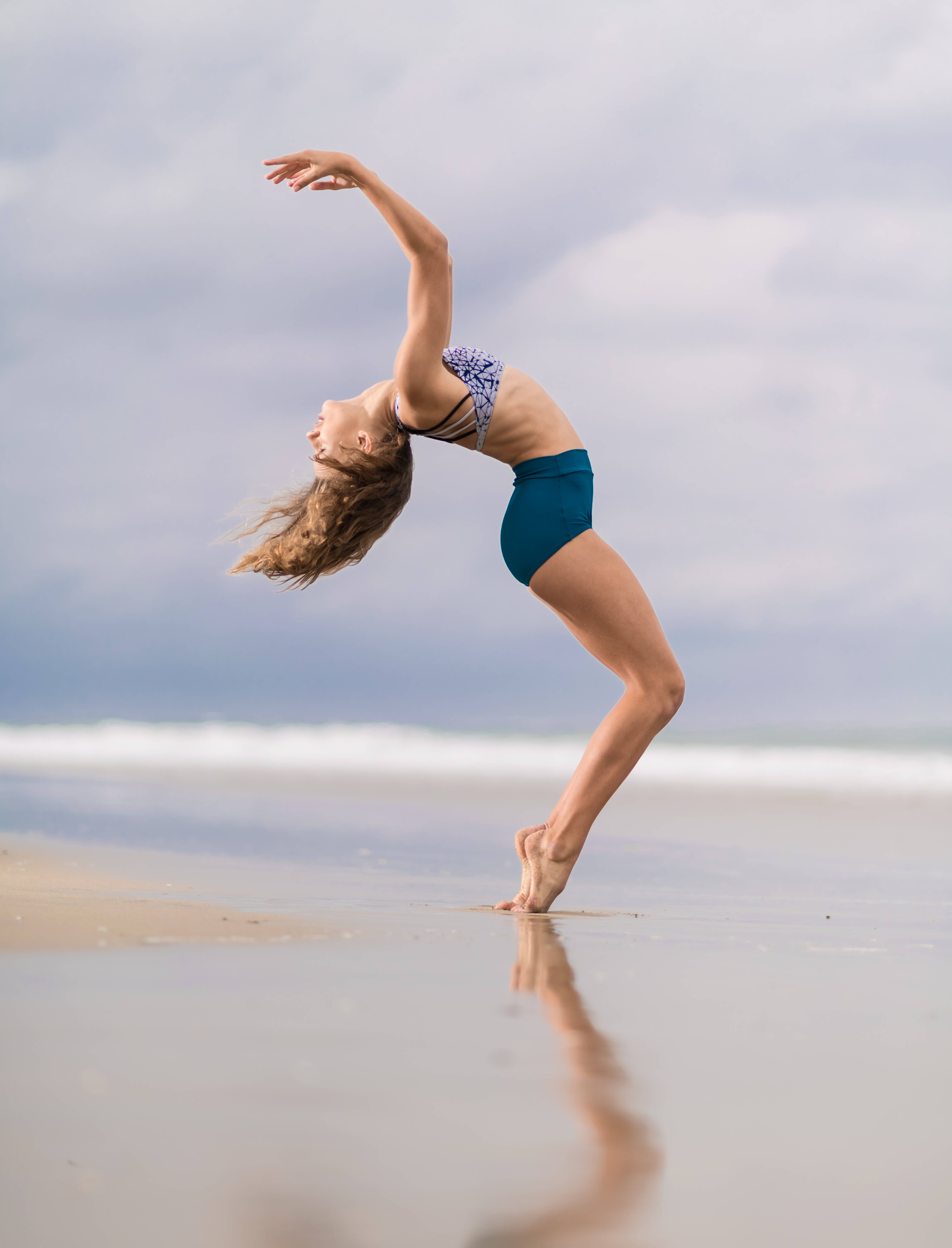 A woman dances on the beach with the ocean in the background. - Gymnastics