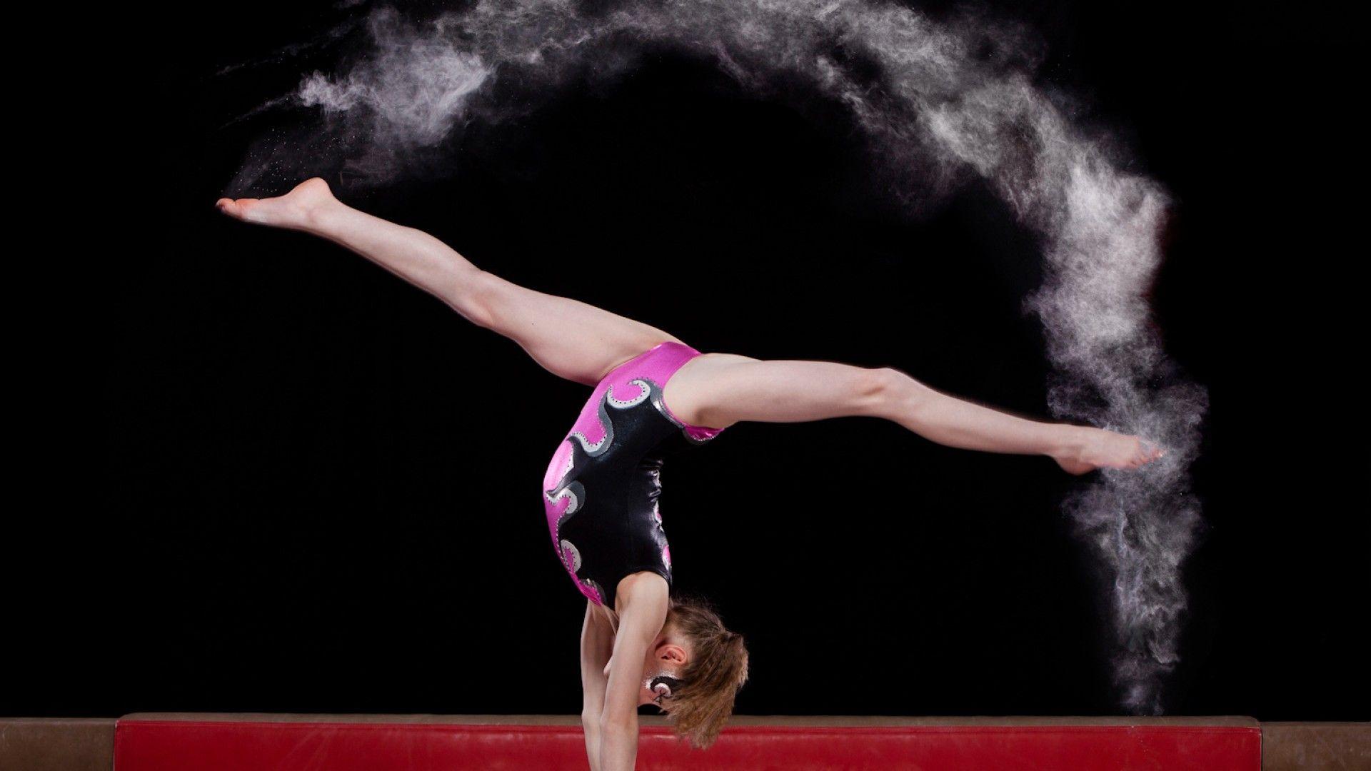 A young gymnast performing a handstand on a balance beam with a cloud of flour behind her. - Gymnastics