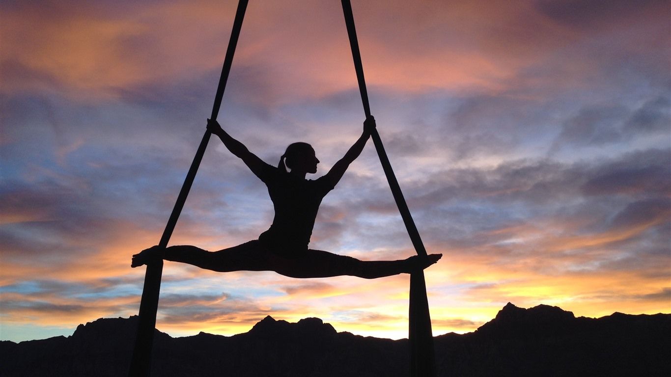 A woman doing aerial yoga against a sunset sky - Gymnastics