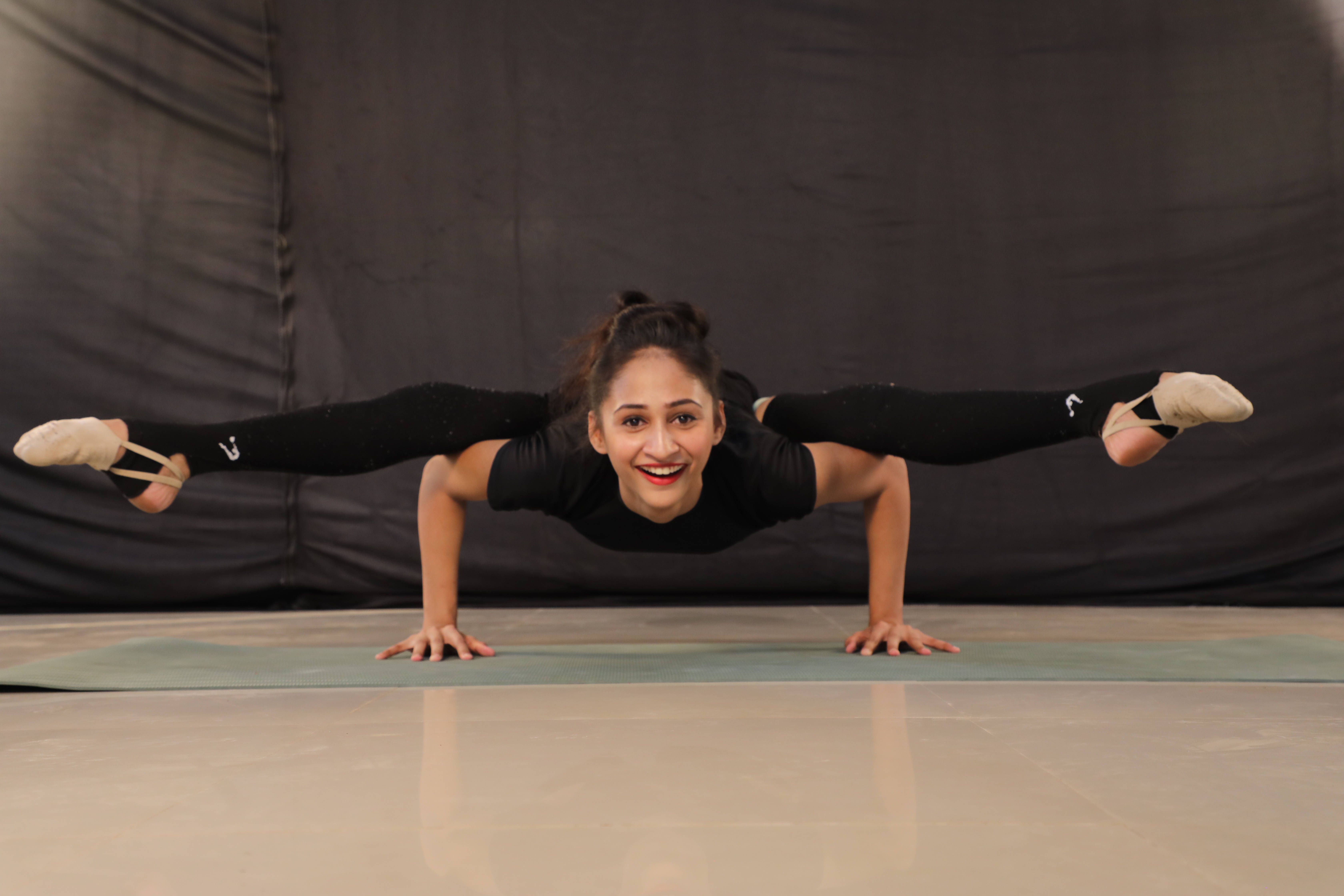 A woman in a black top and tights is doing a handstand with her legs in the air. - Gymnastics