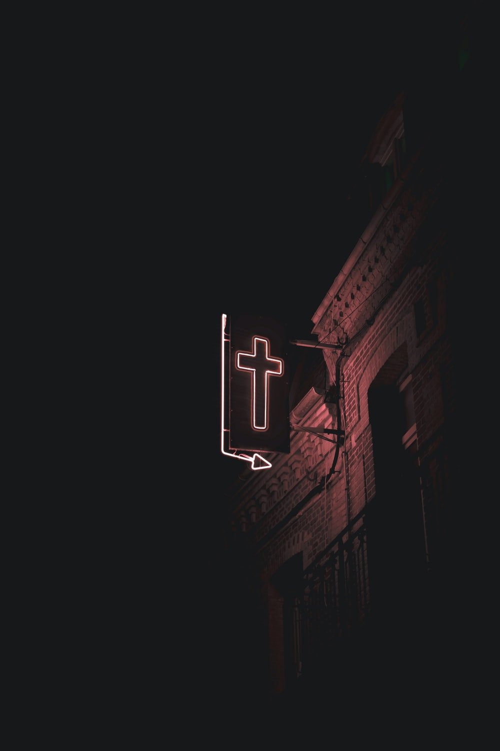 A red neon cross sign on a building at night. - Cross