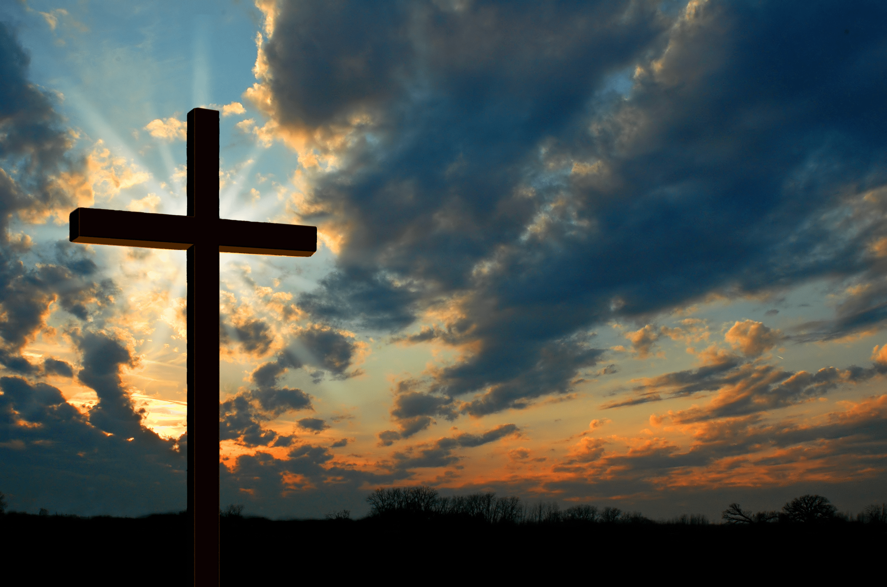A wooden cross stands in front of a dramatic sunset. - Cross