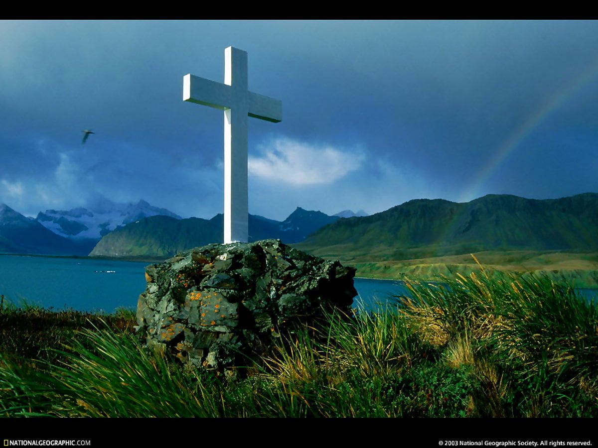 A cross is standing on a rock near a lake. - Cross