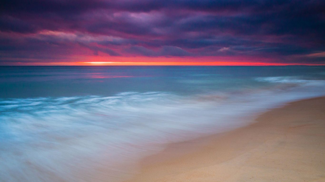 A beach with waves coming in under a red sky - Beach