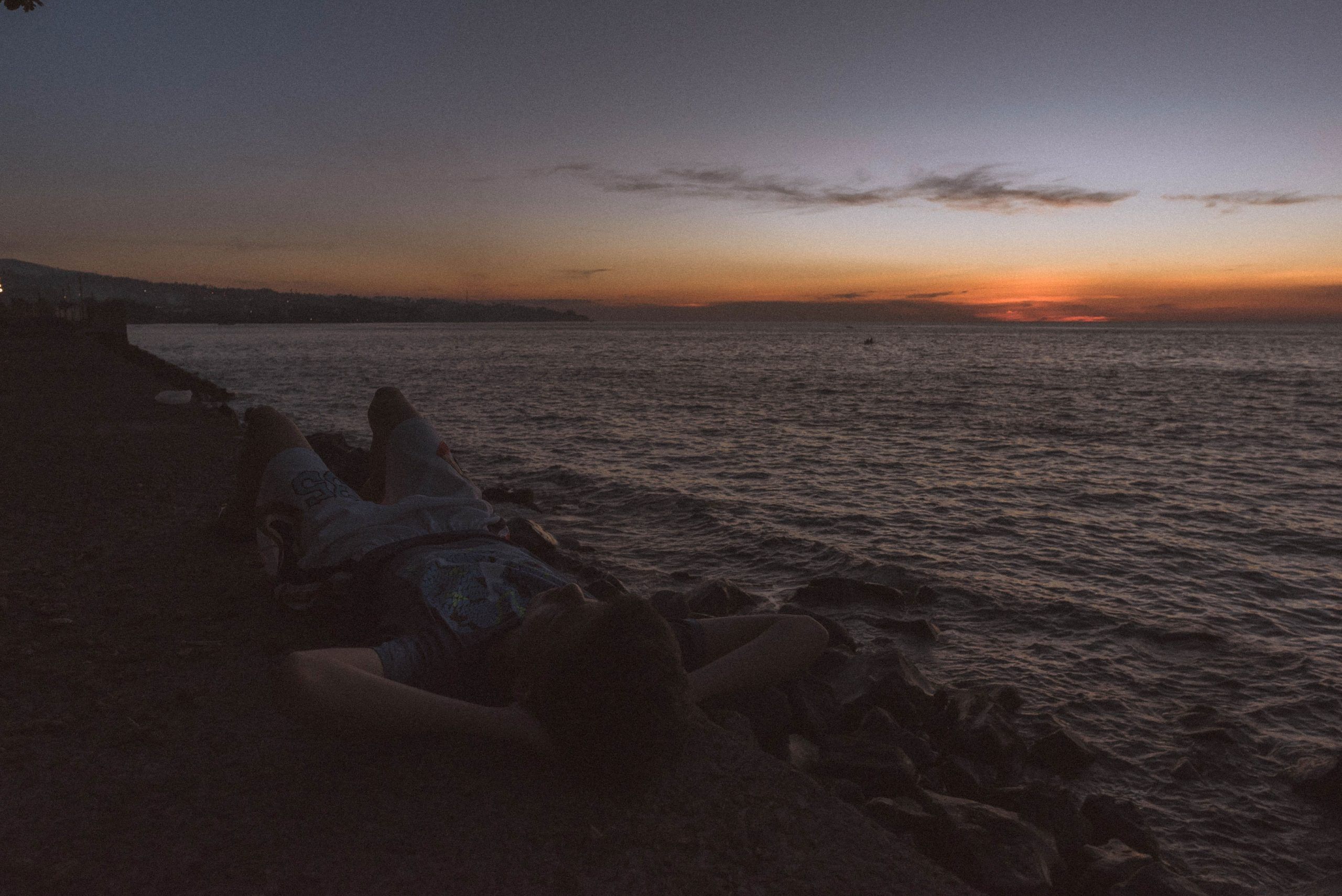 A person laying on the beach watching the sunset. - Grunge