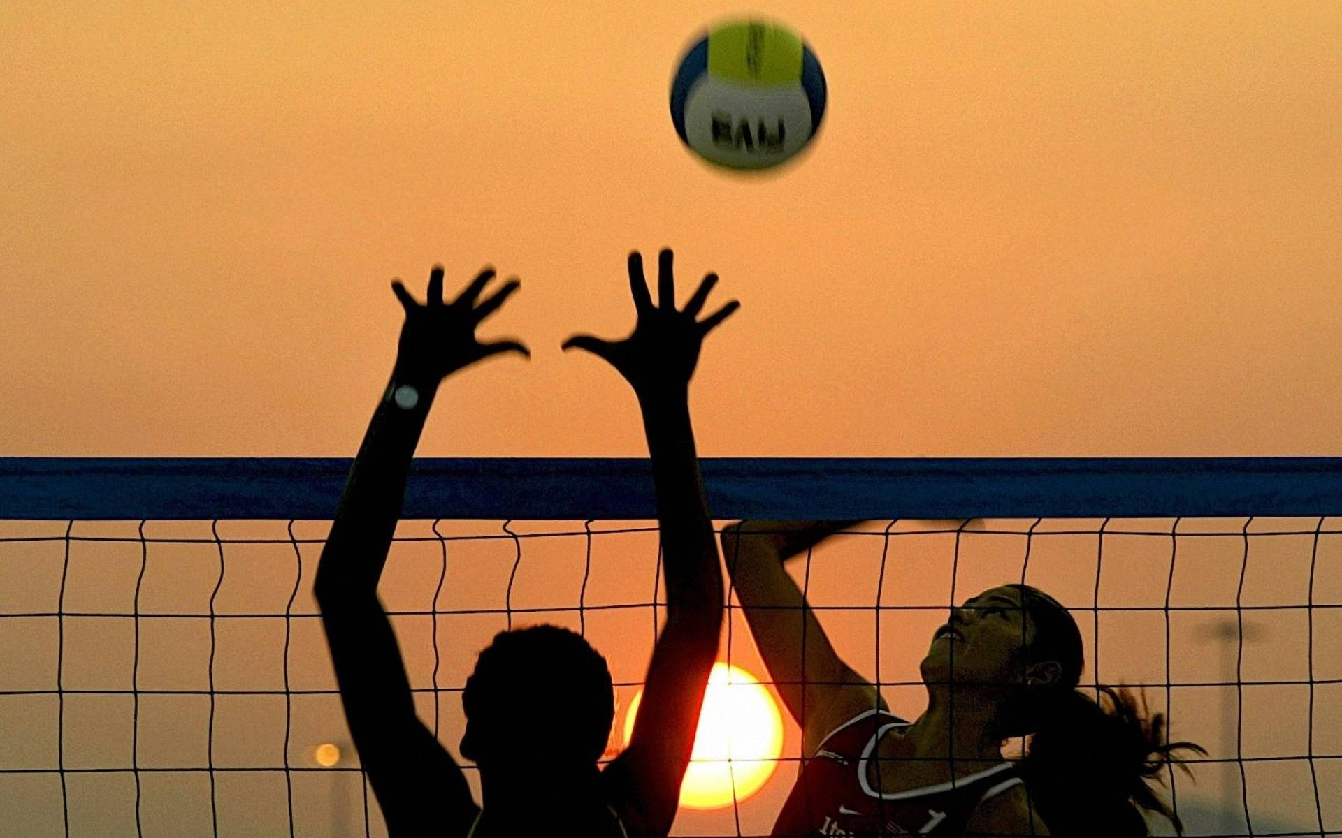 A couple of people playing volleyball at sunset - Volleyball