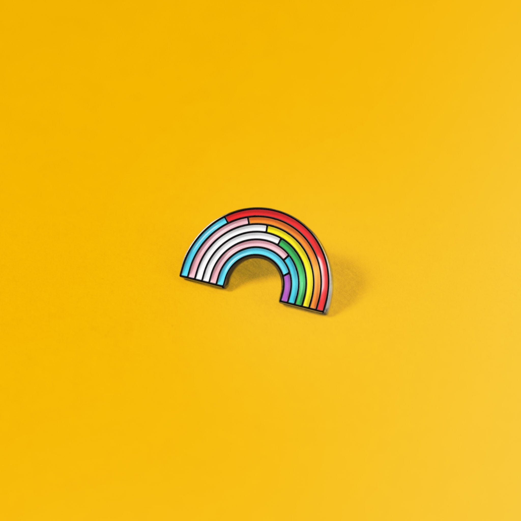 A rainbow shaped enamel pin on a yellow background - Gay, pride