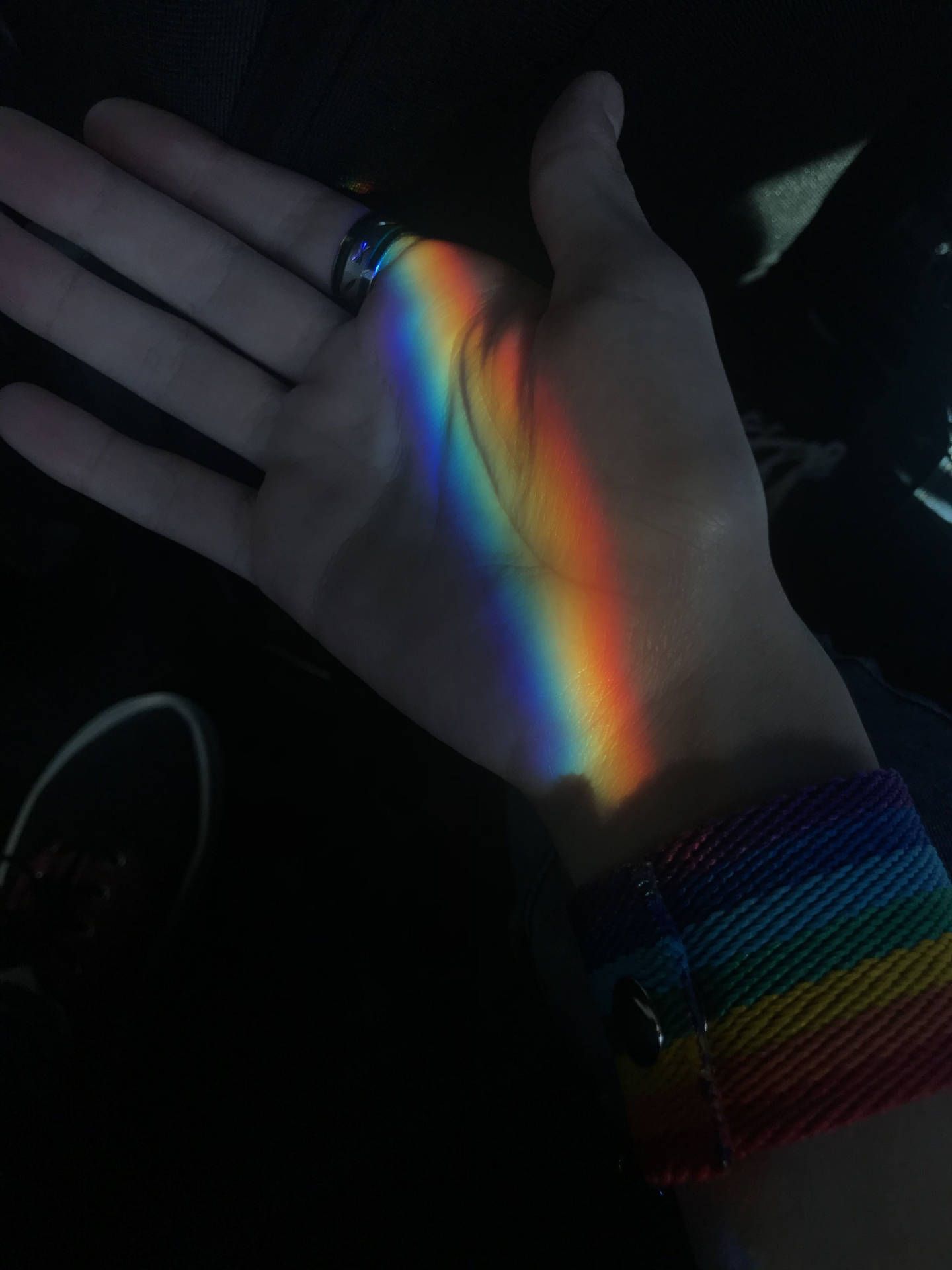 A hand with a rainbow wristband holding a rainbow prism - Gay