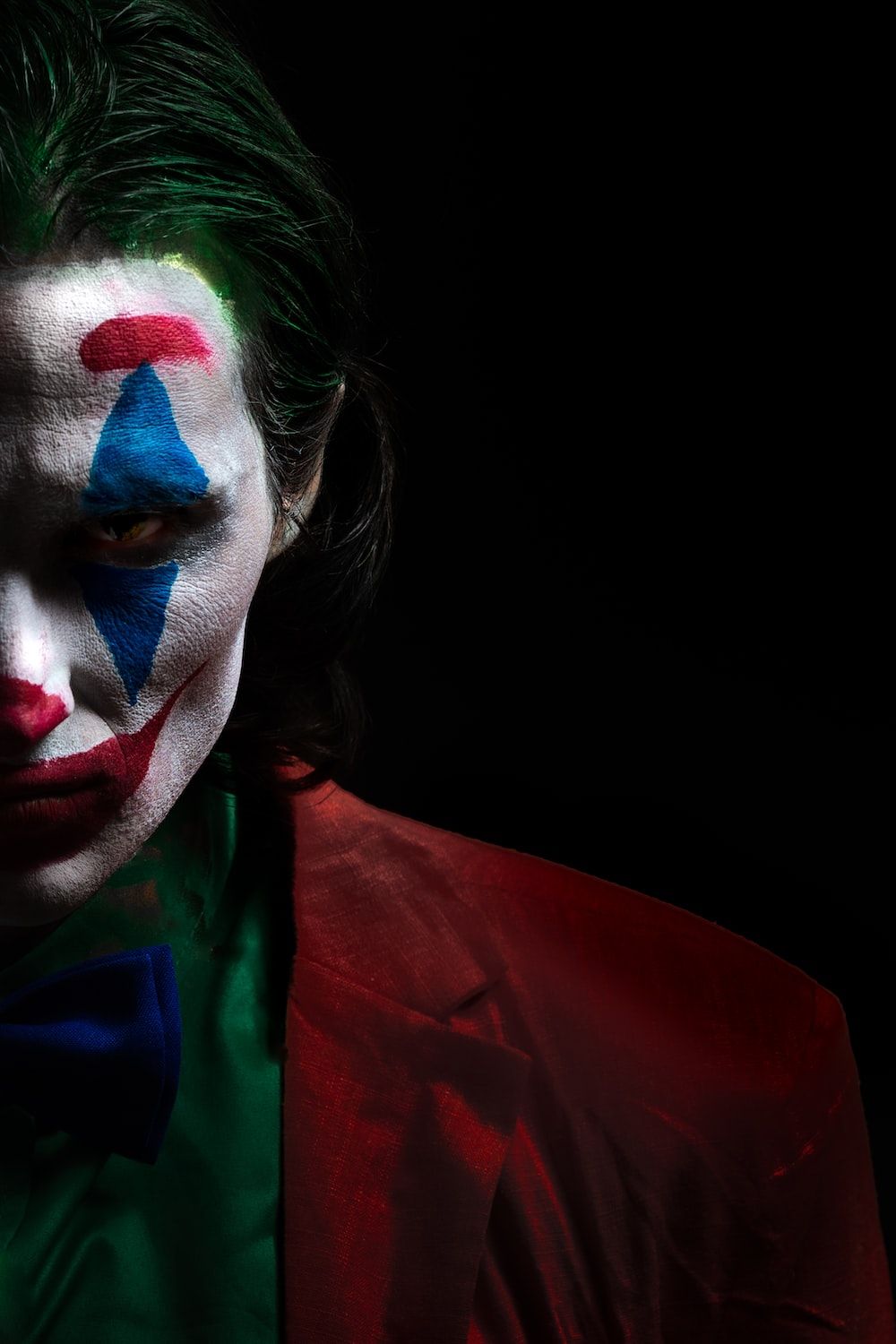 A man with green hair and clown makeup on his face. - Clown