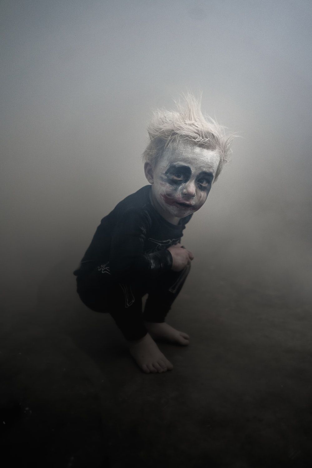 A child in clown makeup squatting down - Clown