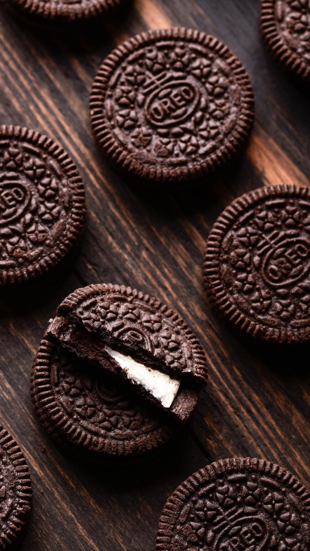 Oreo cookies on a wooden table with one cookie broken in half. - Oreo