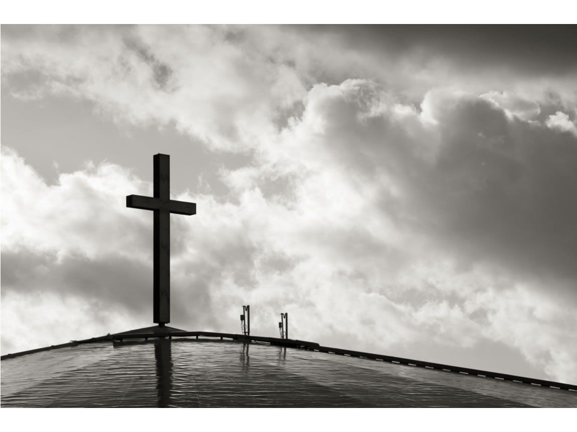 A cross on top of a building with a cloudy sky in the background. - Cross